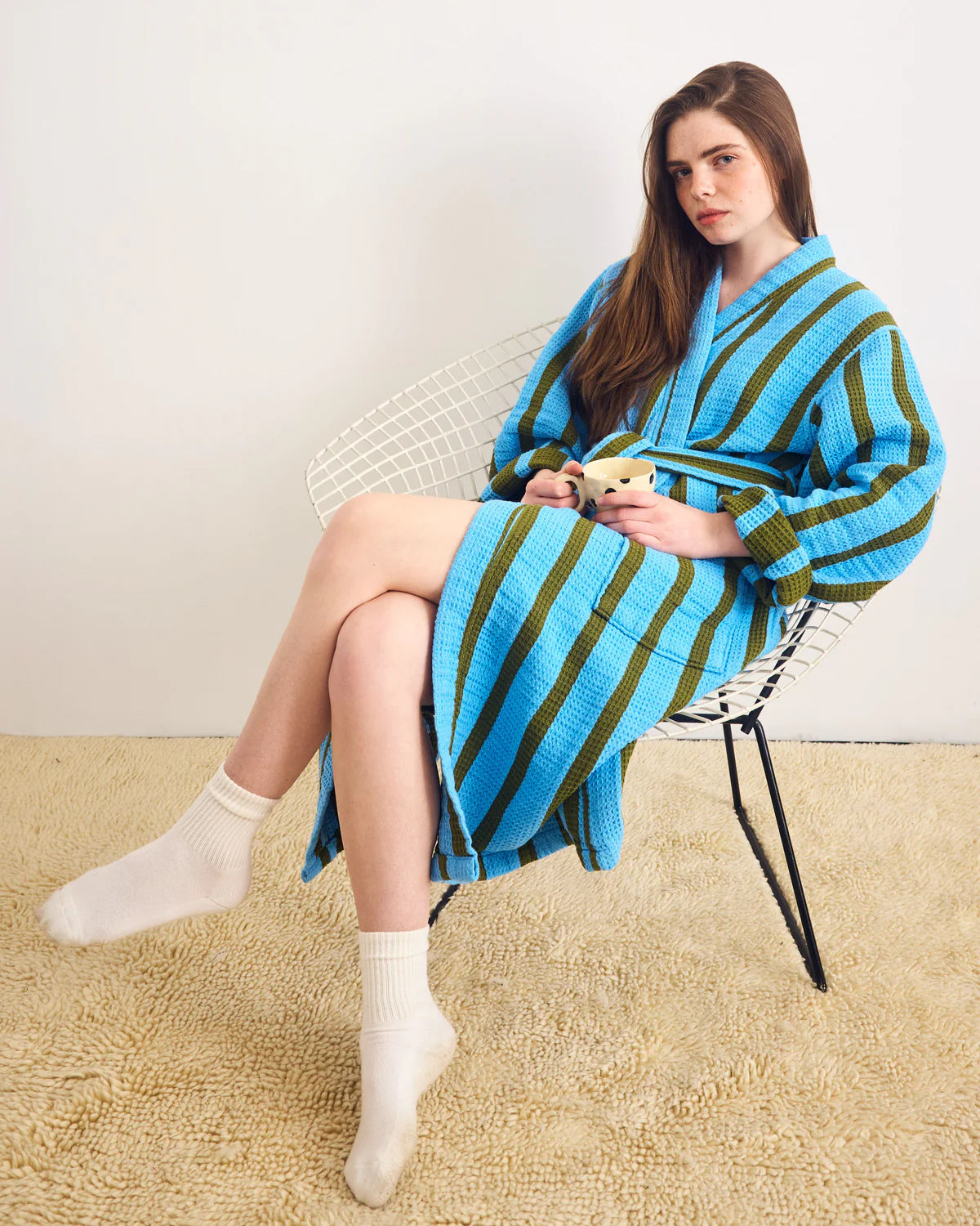 Woman sitting on a chair wearing a blue and green striped robe.