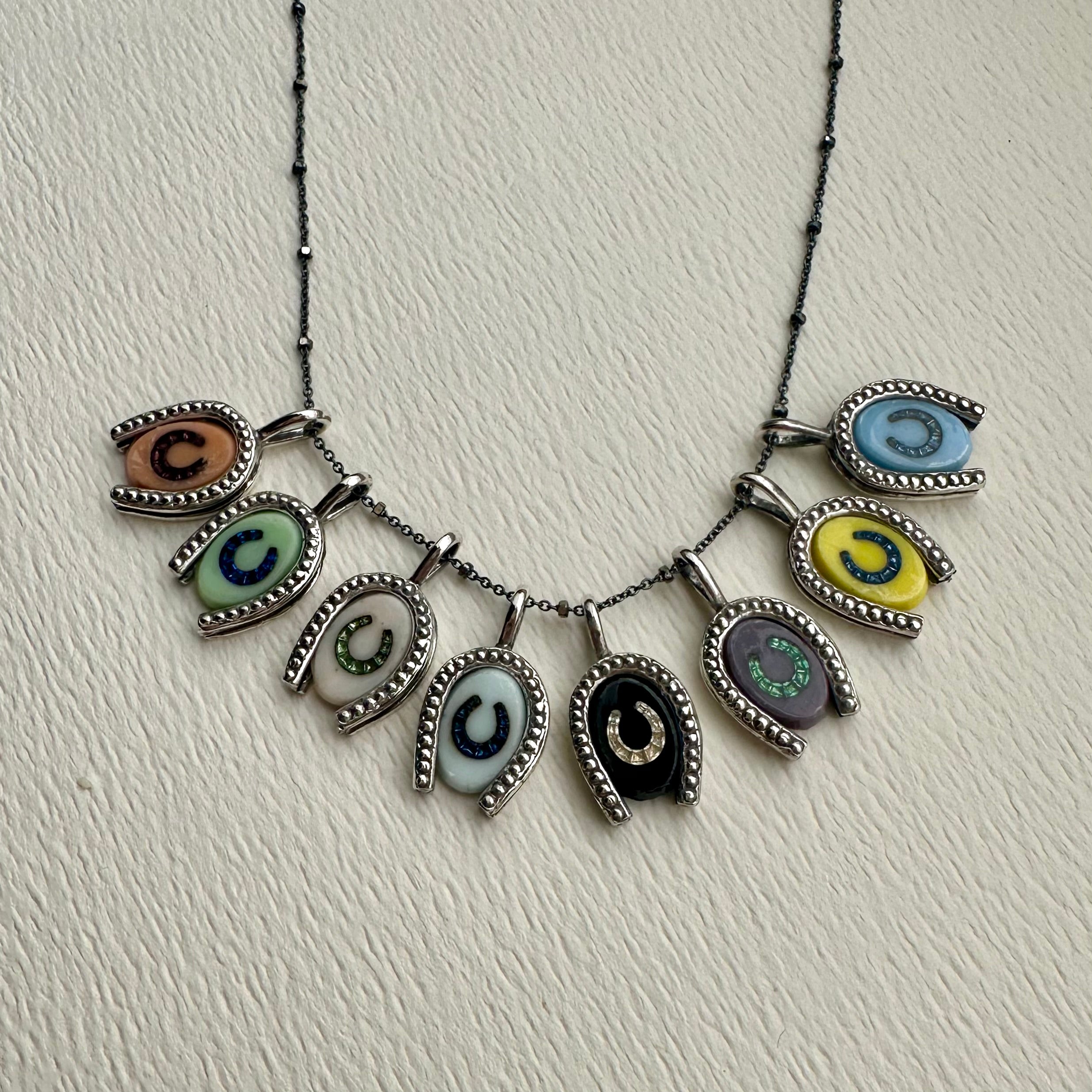 Eight different glass intaglio horseshoe charms with various colors of rhinestone inlay hanging from 18" silver chain.