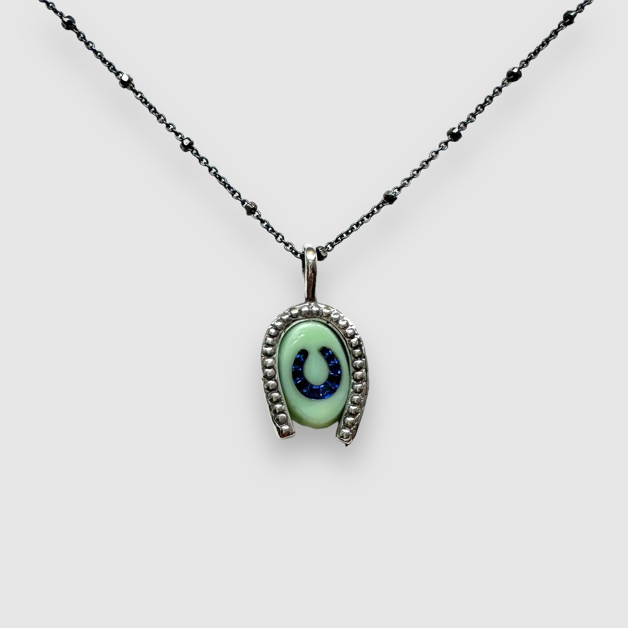 mint green glass intaglio horseshoe charm with blue rhinestone inlay hanging from 18" silver chain