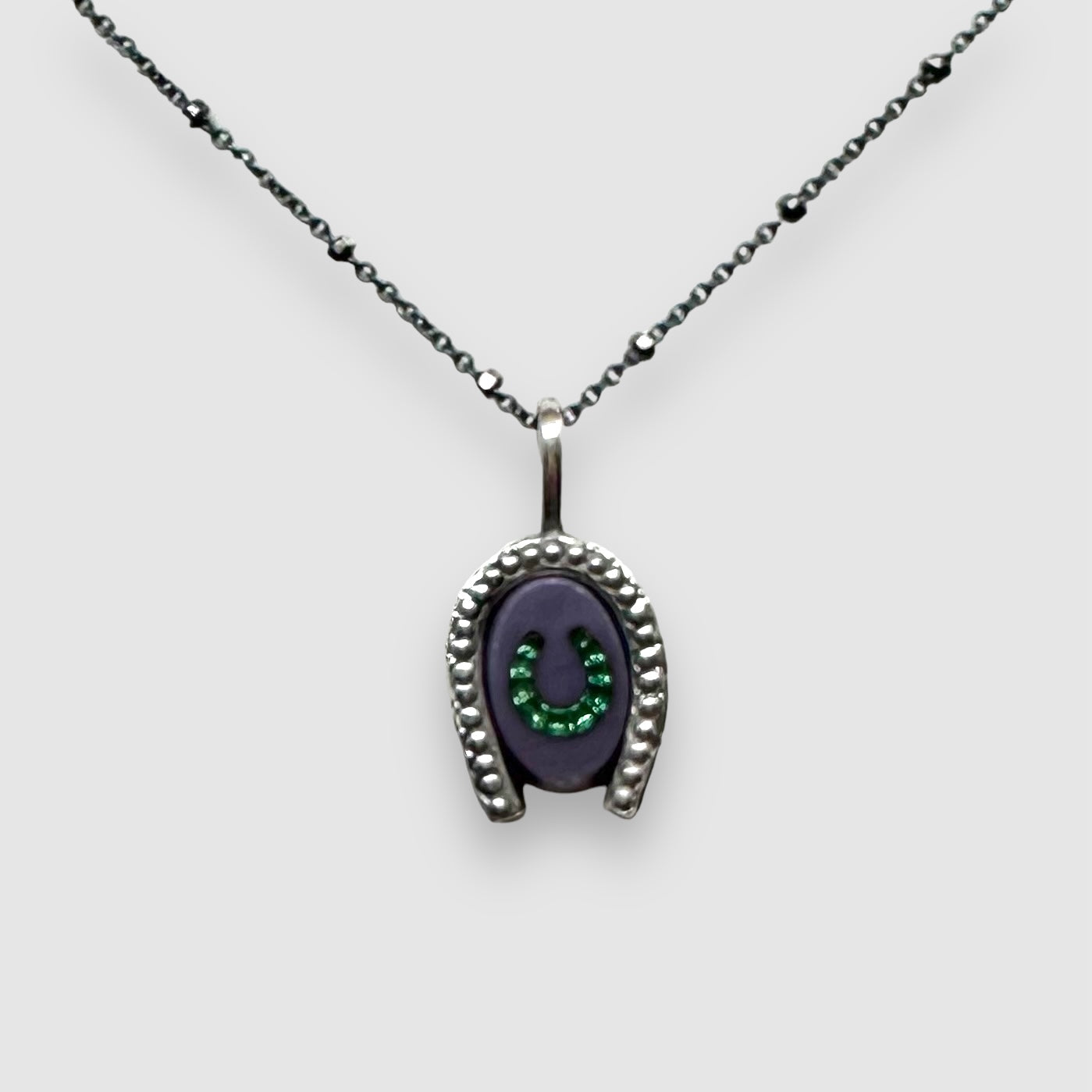 purple glass intaglio horseshoe charm with green rhinestone inlay hanging from 18" silver chain