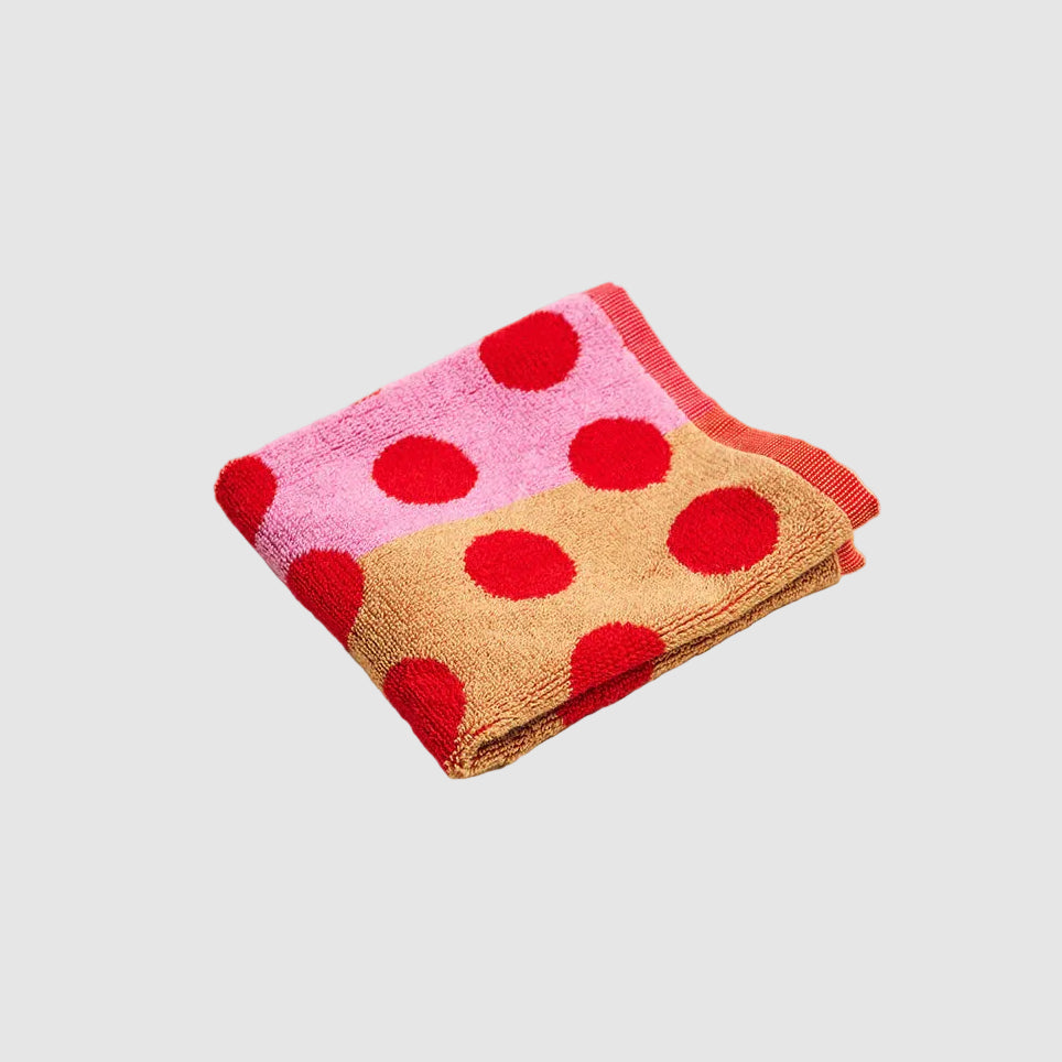 Folded fabric with pink, red, and beige polka dot pattern on a beige carpet.