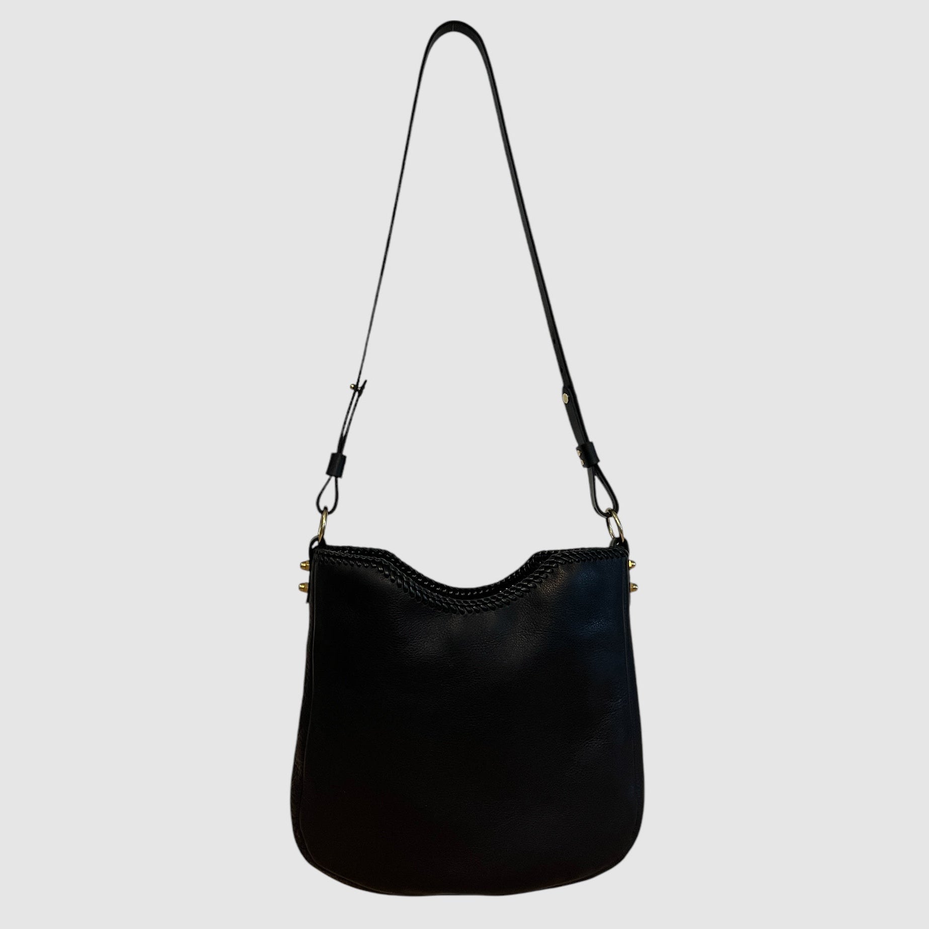 Black leather crossbody bag with an adjustable strap and brass details, photographed against a white background.
