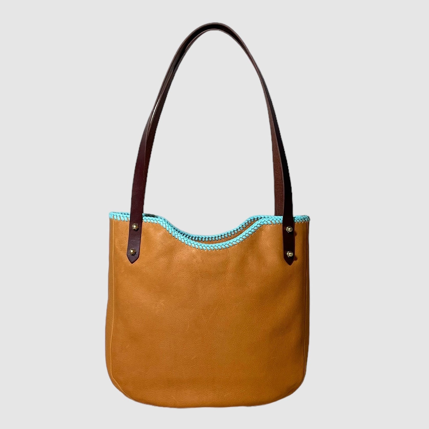 A shoulder bag with a dark honey and soft turquoise leather, featuring brass hardware and a light turquoise leather lacing detail at the top