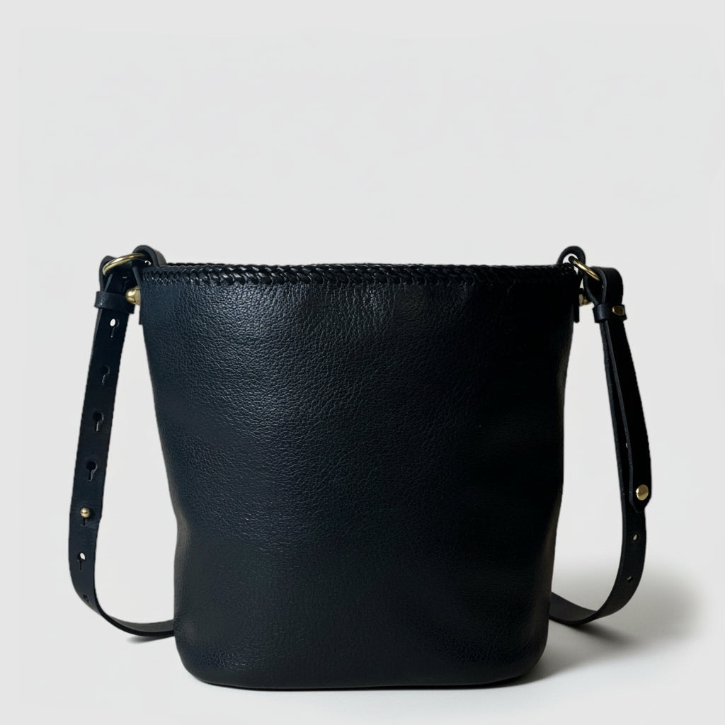 A charcoal gray bucket bag with black leather lacing and an adjustable leather strap, displayed against a plain background.