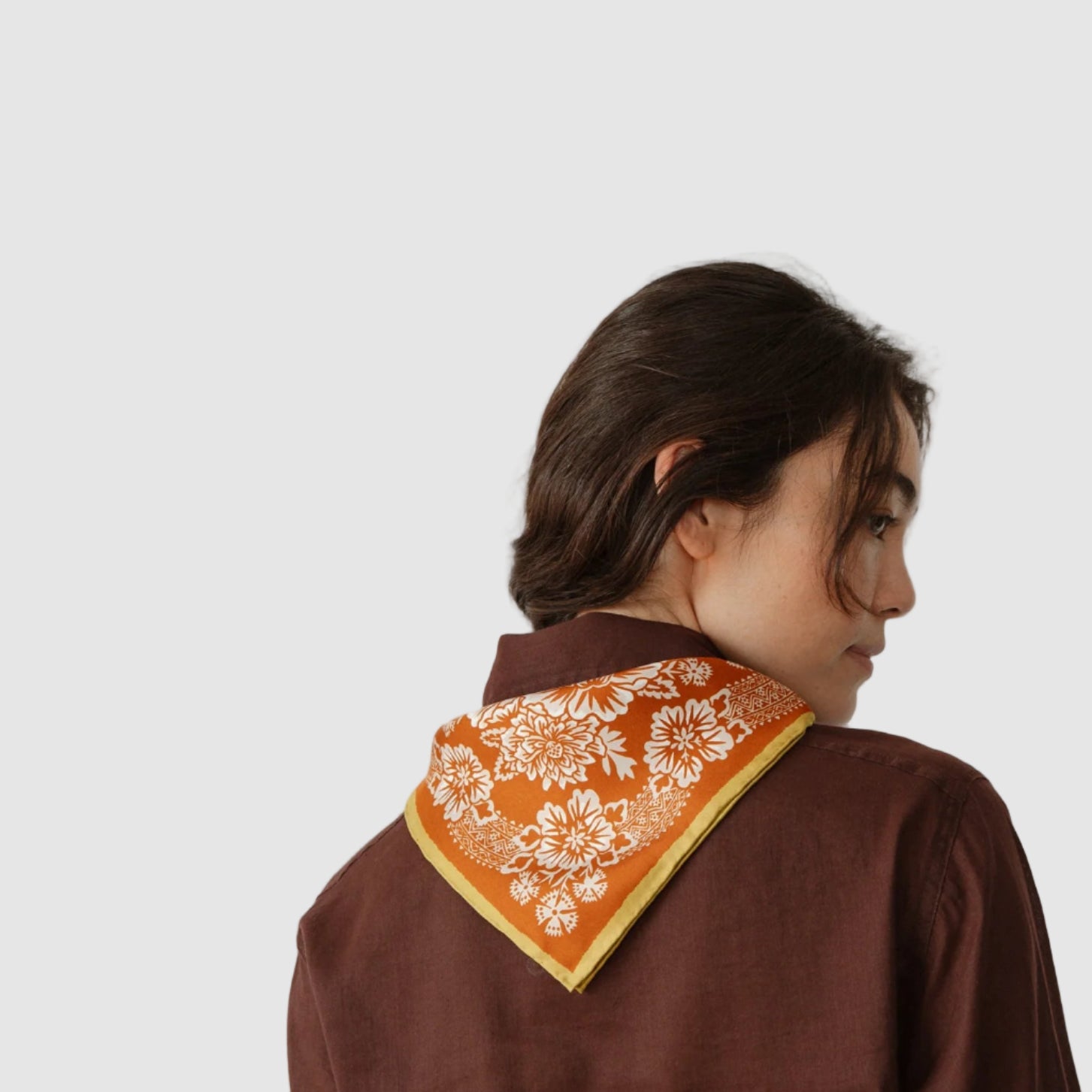Person wearing a brown garment with an orange and white patterned scarf on a plain background