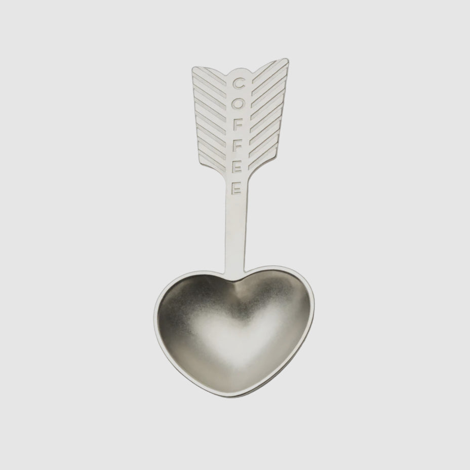 A silver-colored, heart-shaped coffee spoon with an engraved arrow handle, presented against a white background.