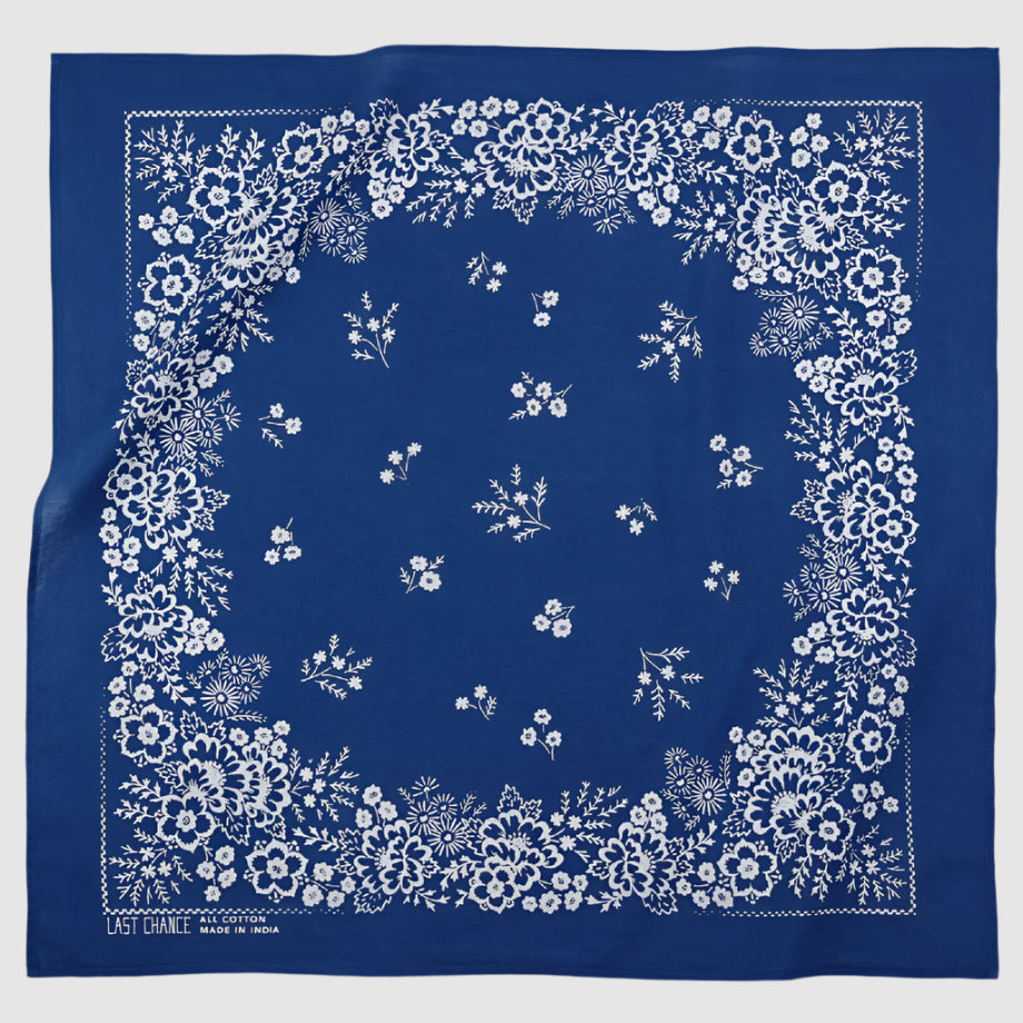 Blue and white, classic Western-Wear Bandana. A floral pattern is centered on blue bandana printed in white. Pattern is floral-like and described as being inspired by California's super bloom, french sample books, and the town of Zalipie, Poland. 22x22 in.