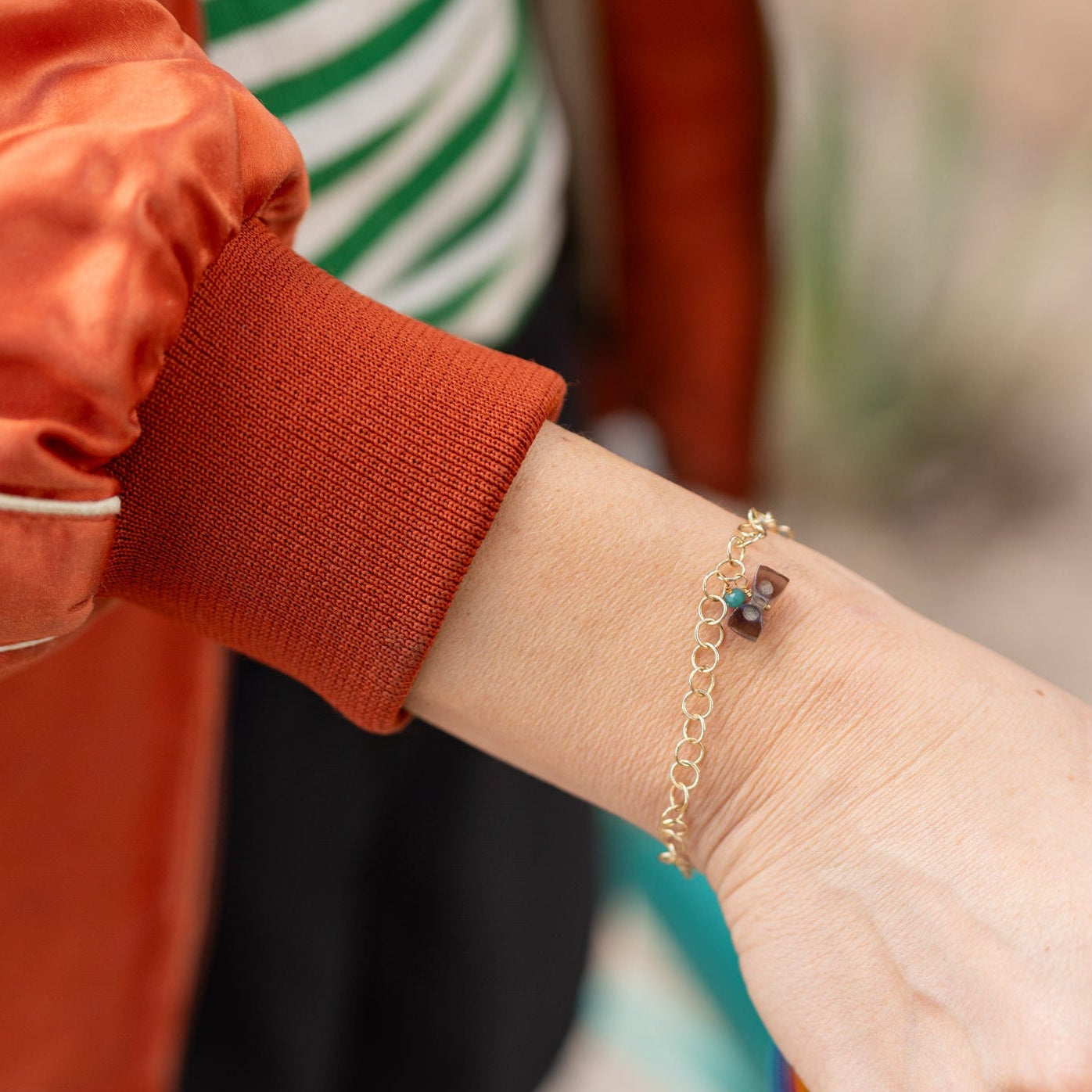 Person wearing chain bracelet with carved bow charm and silver starburst signet ring with a blurred background