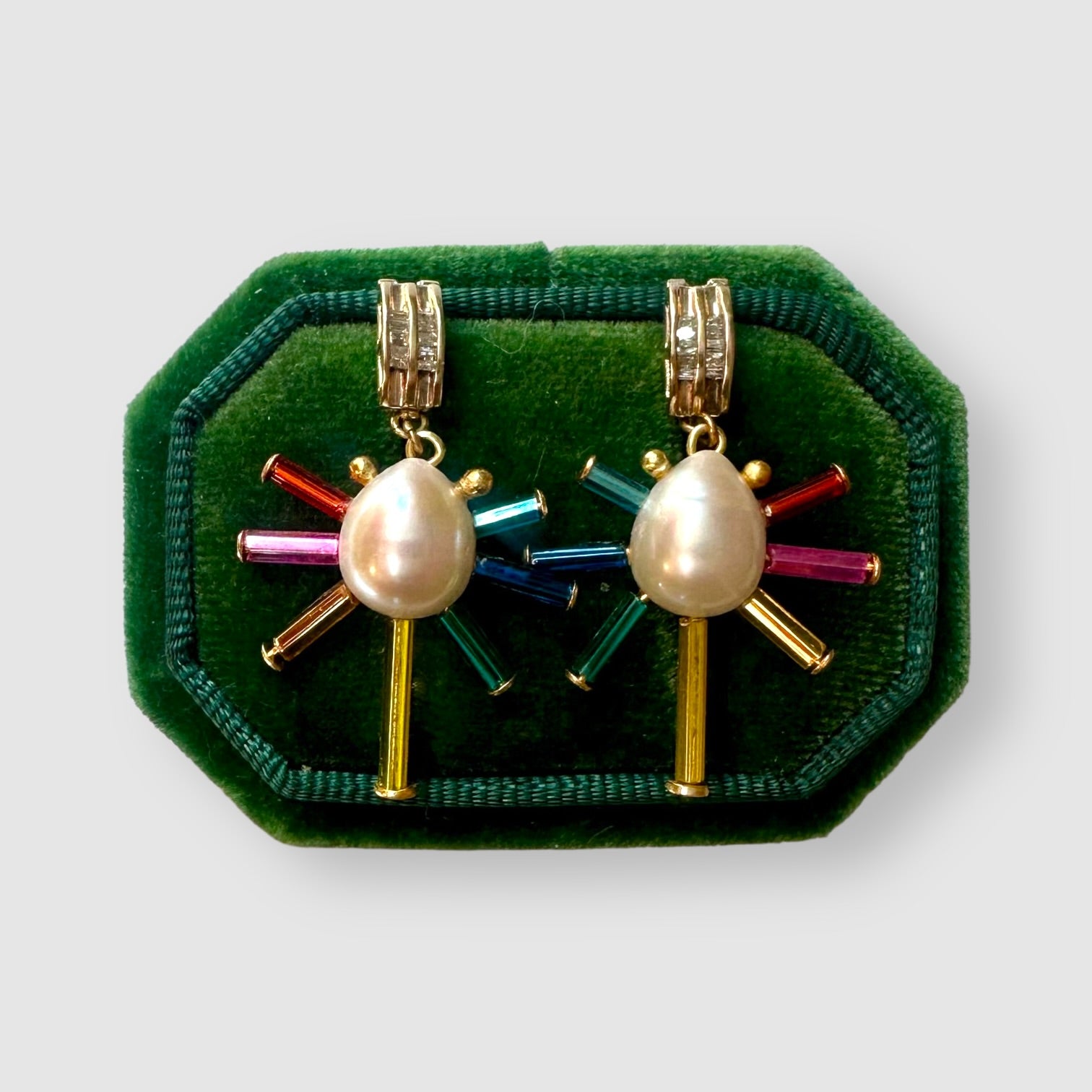Pair of earrings handmade by Sofie Albertsen in Tucson, Arizona. Pearl center with vintage glass beads strung on a vintage diamond bracelet piece. Displayed on a green cushion on a light grey background.
