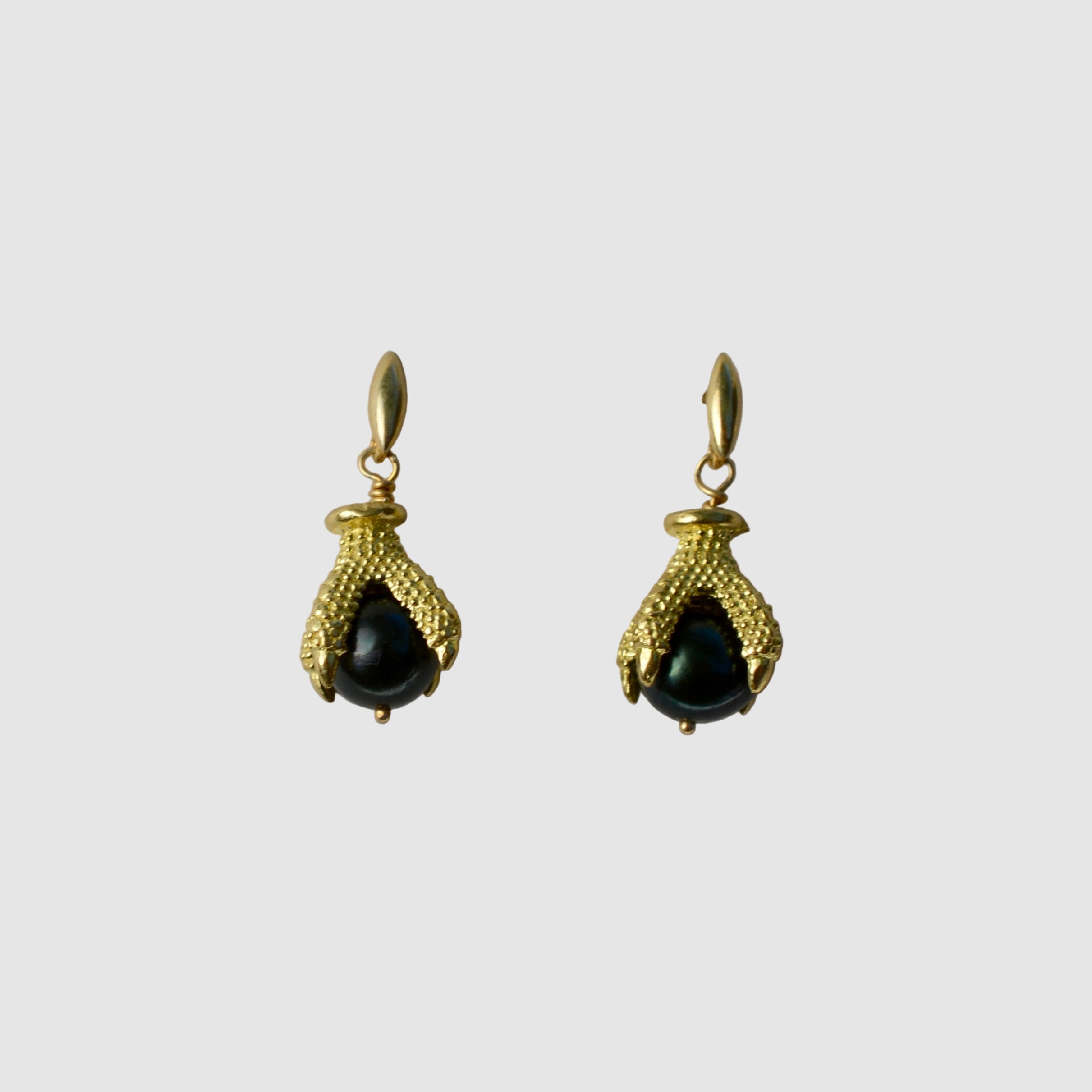Gold talon earrings with black pearl on a light gray background