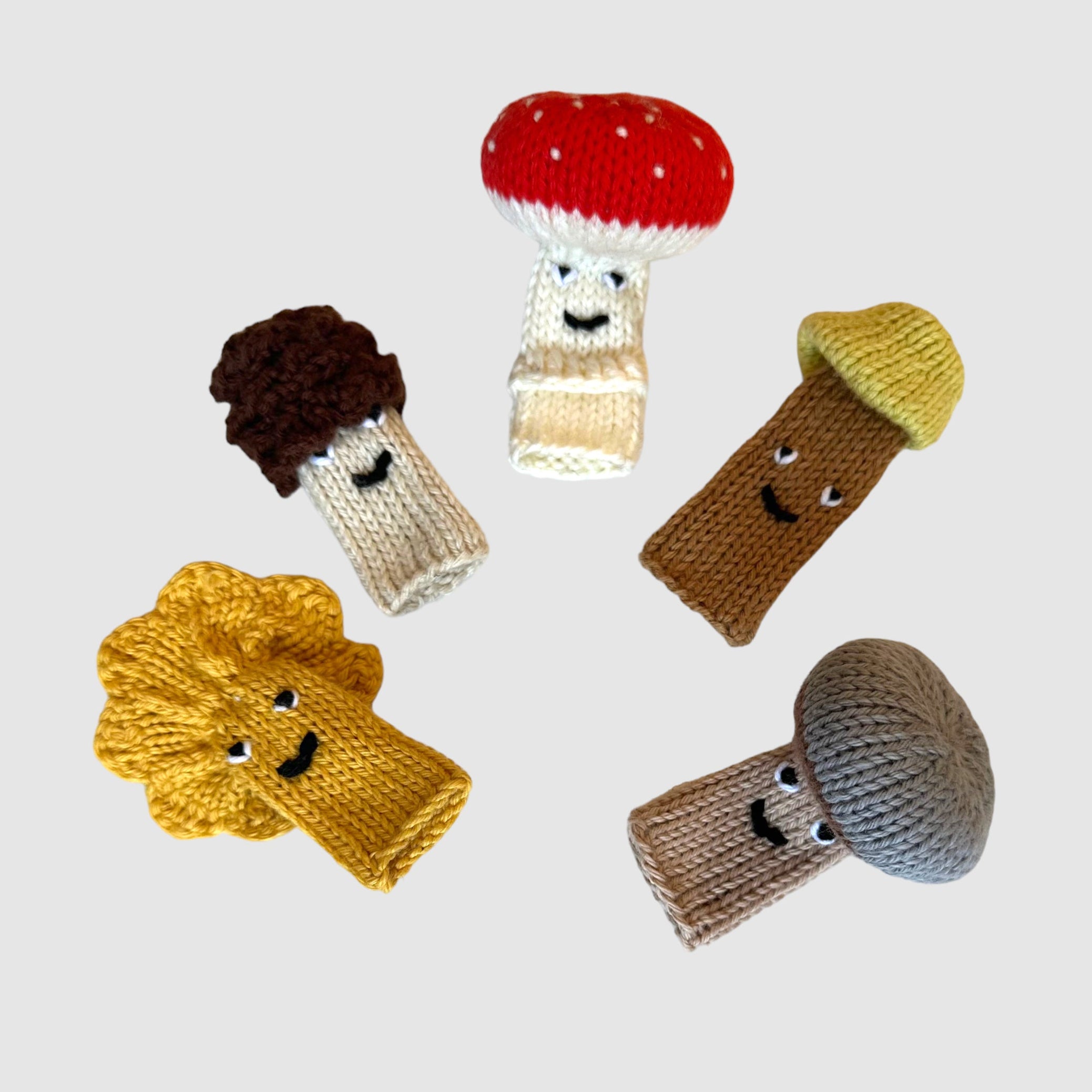 A set of five knitted finger puppets designed to look like mushrooms, with varying colors and expressions.