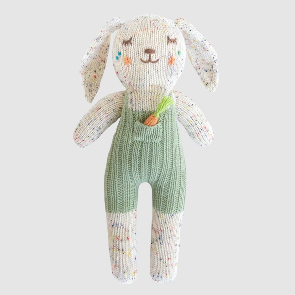 A plush toy rabbit made of cotton knit fabric, primarily in beige with green overalls and a carrot decoration.