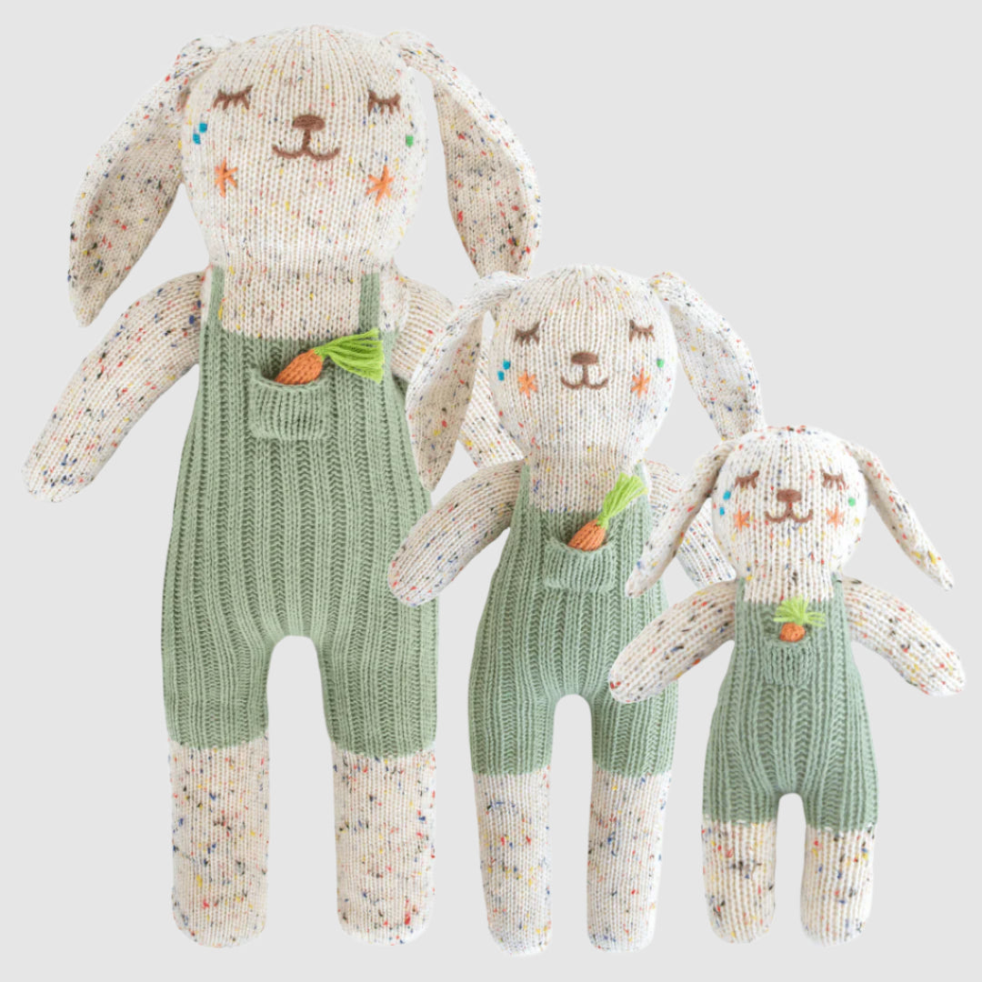 Three knitted bunny toys with green overalls on a white background