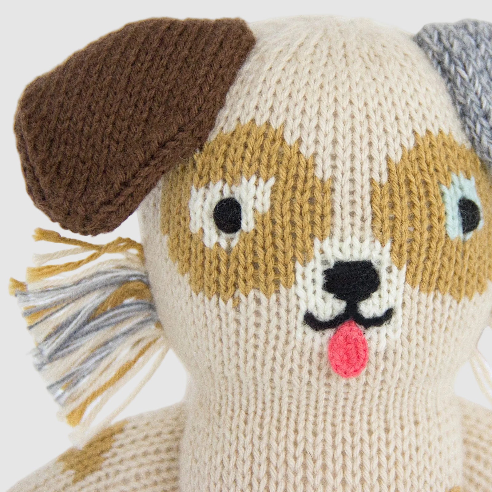 Close up of an Ozzie the Dog handmade knit doll from BlaBla Kids on a light grey background