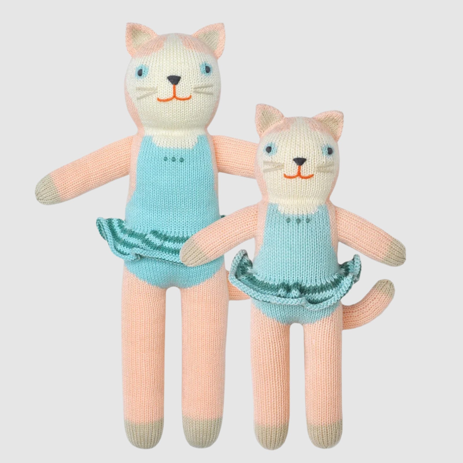 Two knit dolls shaped like cats with blue dresses and beige bodies, the larger doll standing upright and the smaller one lying down.