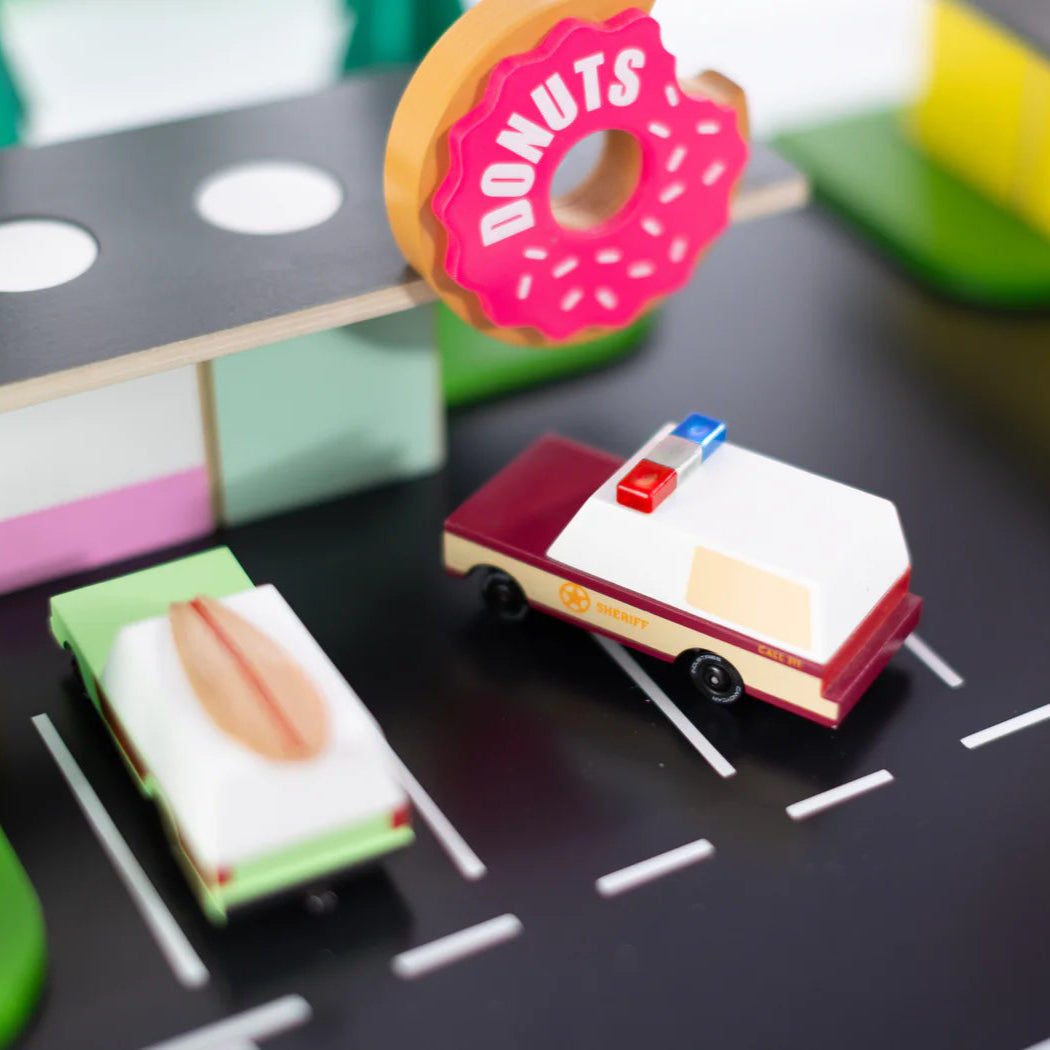 Toy cars on a miniature road with a donut-shaped sign in the background