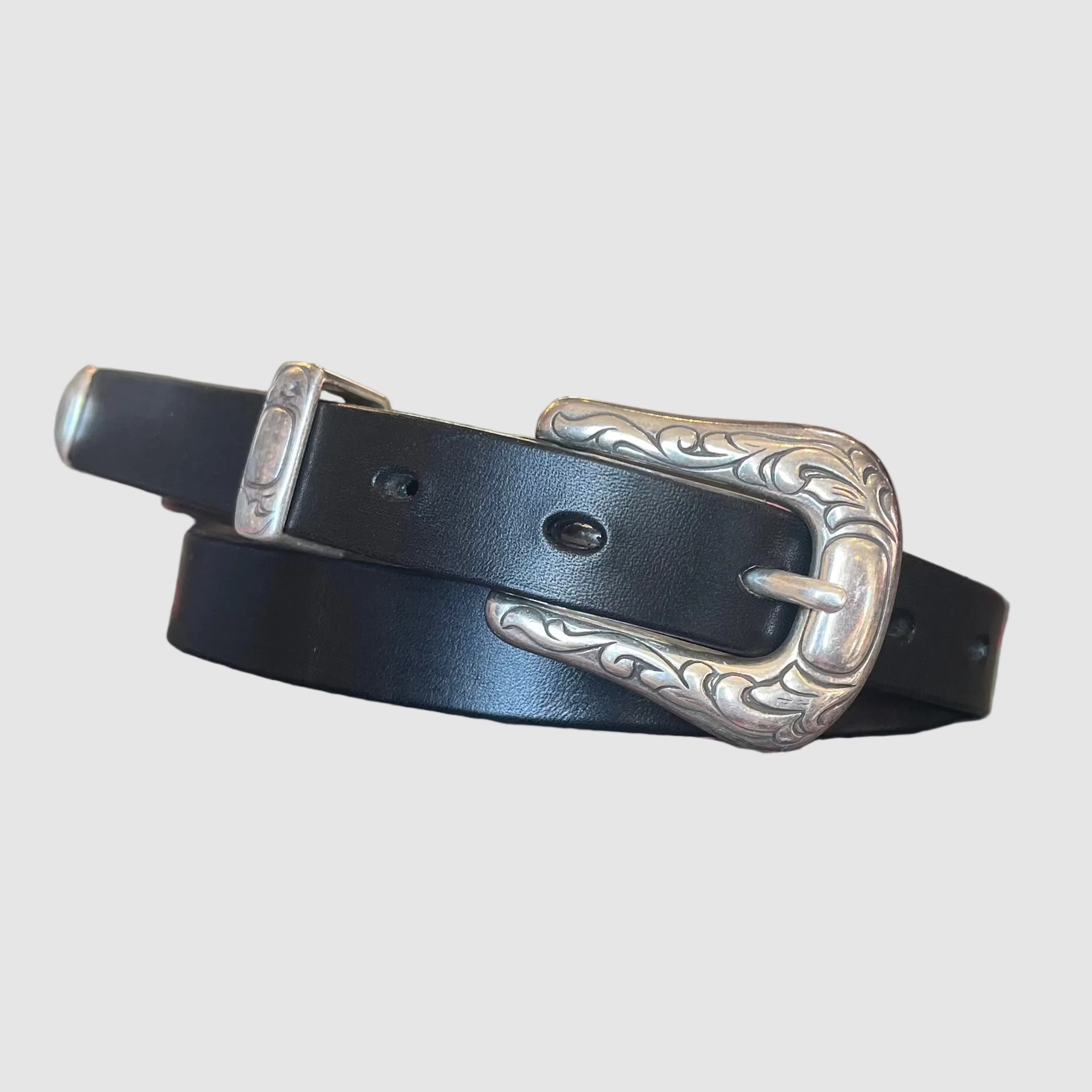 Black, handmade, leather belt with silver ornate buckle on a light grey background