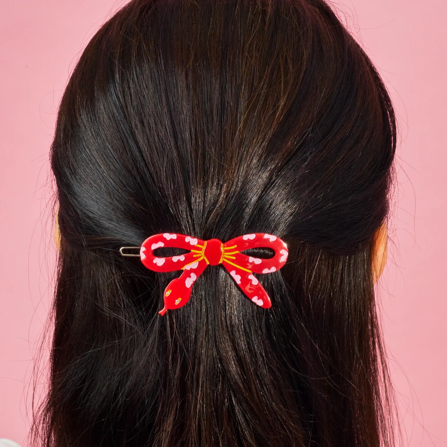 A "year of the snake" styled Centinelle barrettein a young person's dark brown hair. Light pink background