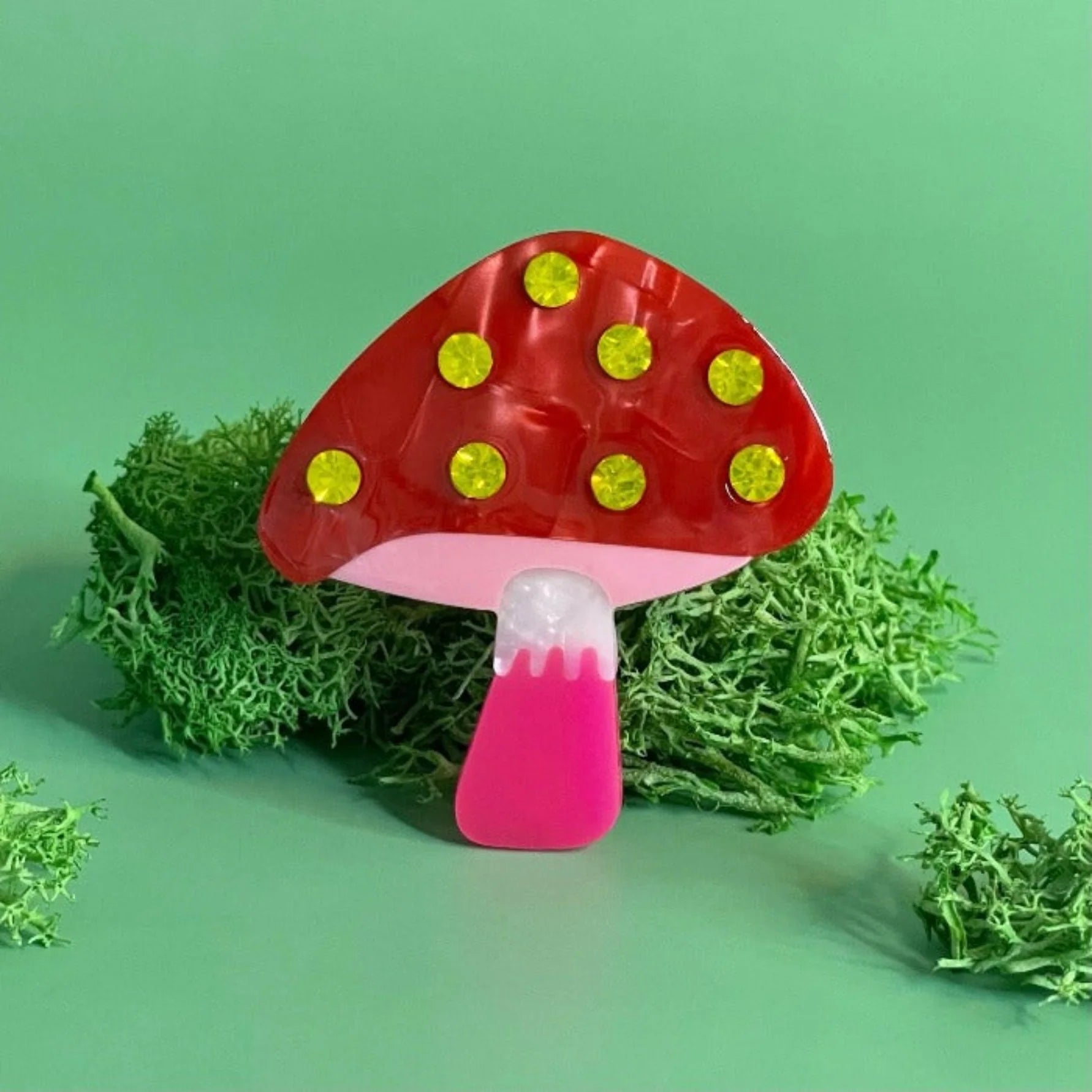 A Centinelle, 'mushroom' style barrette on a light green background with some moss in the back