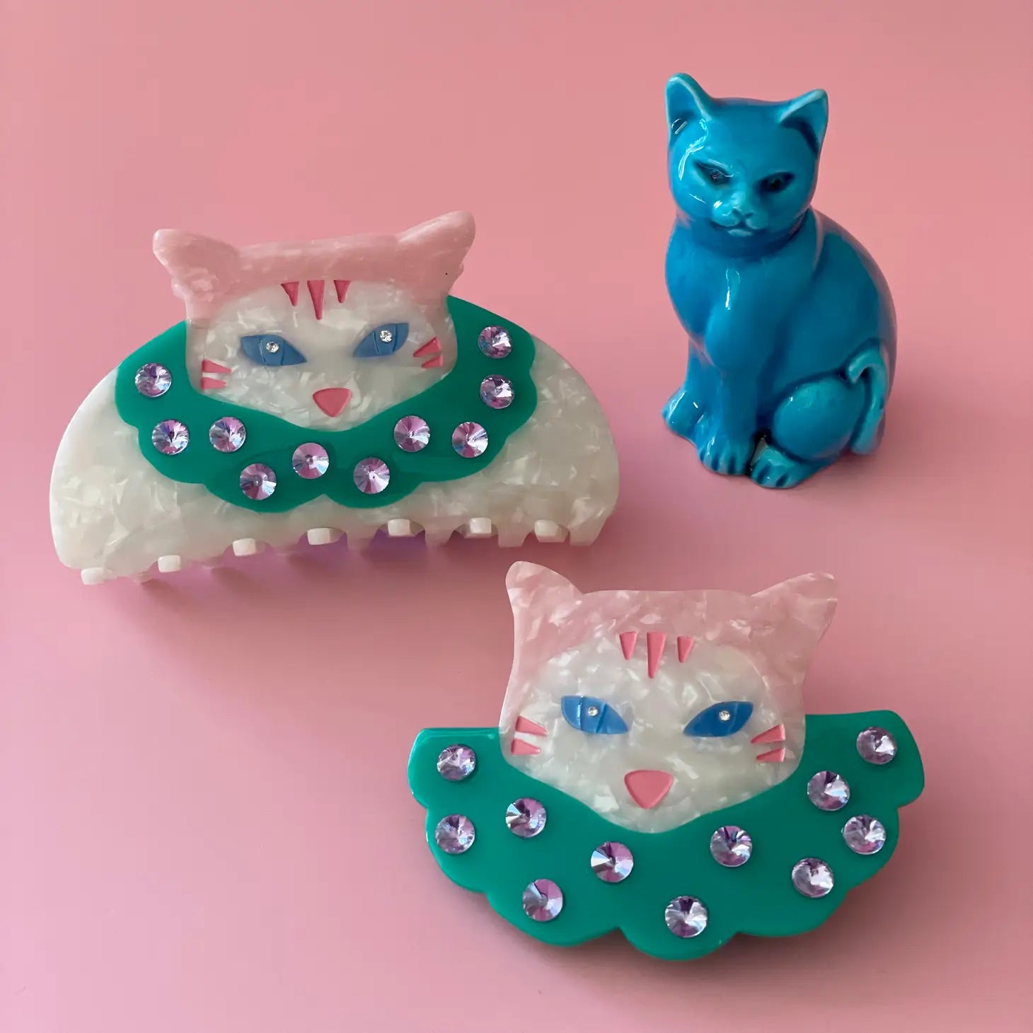 A couple Centinelle hair claw clips with a cat clown design on a light pink background.