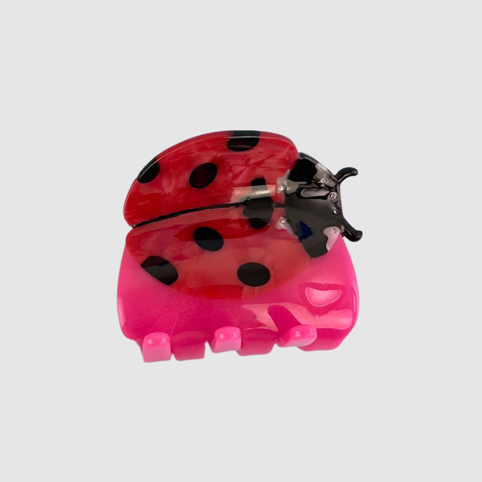 Pink, red, and black ladybug hair claw clip on a blank grey background.