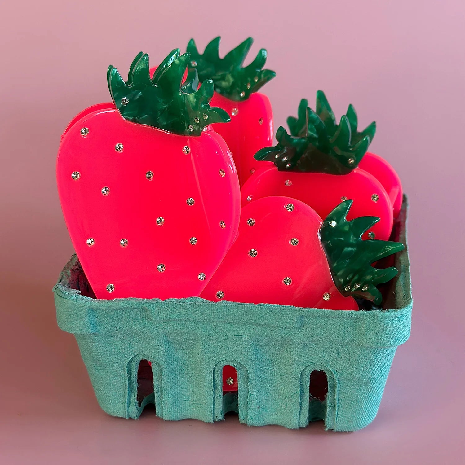 'Neon strawberry' styled Centinelle hair claw clips in a blue, cardboard strawberry carton. light mauve background