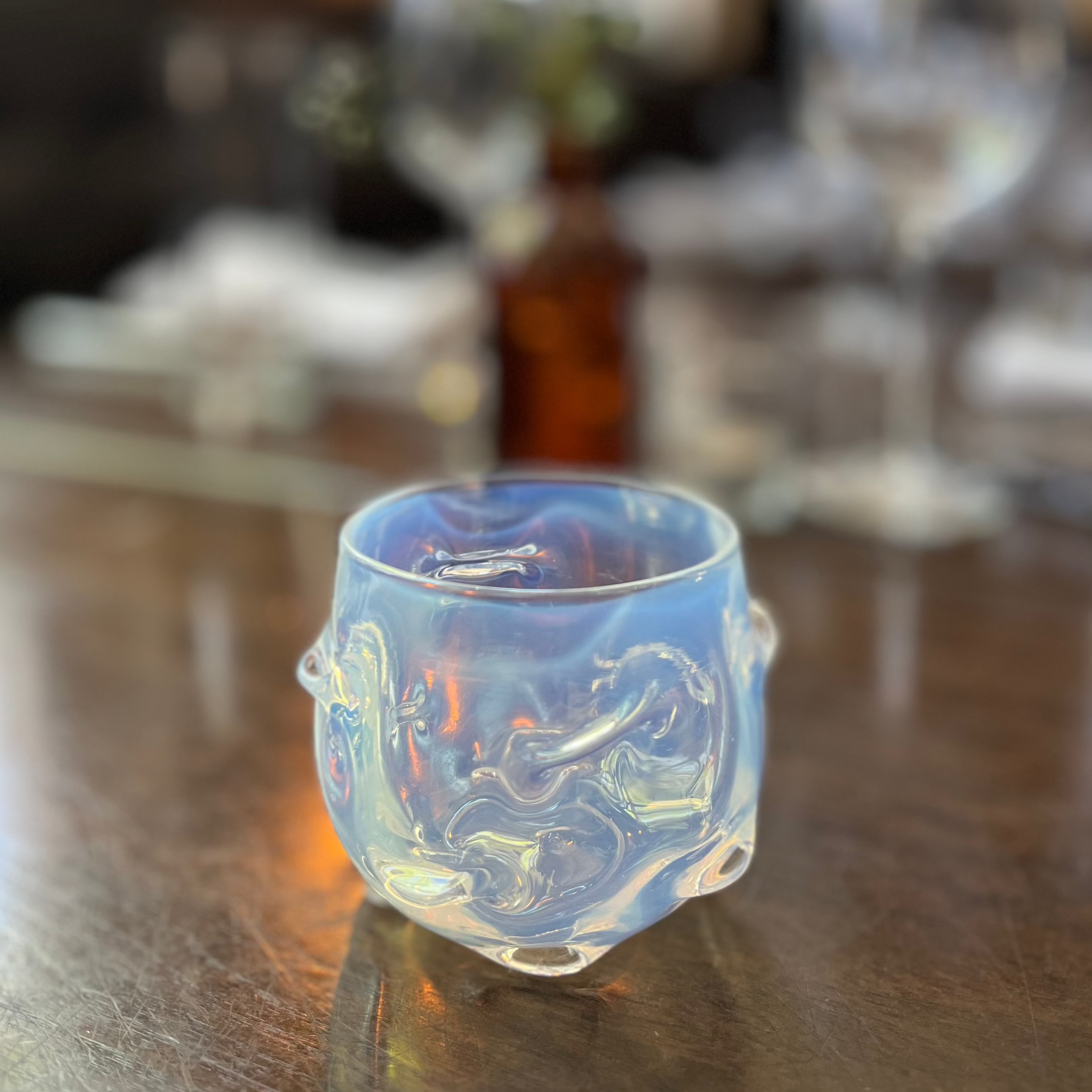 Opalescent glass cup on a wooden table with blurred background.