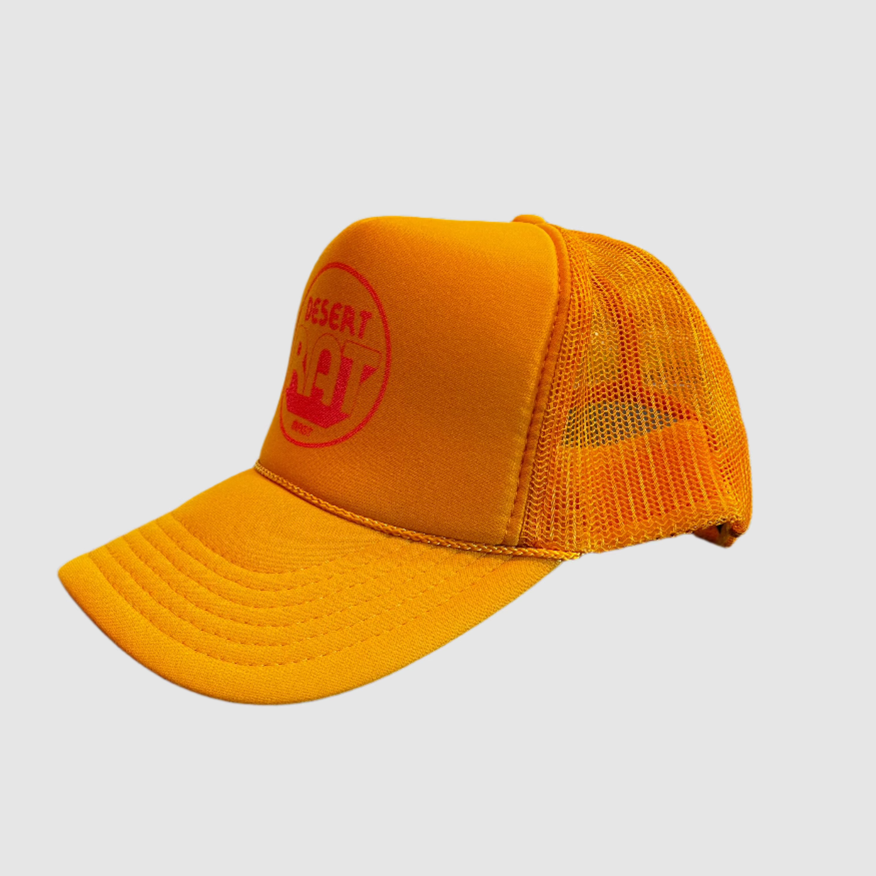 Front view of a side view of a yellow truckers cap with a pink, circular "desert rat" logo on front with "MAST" small underneath logo. Light gray background