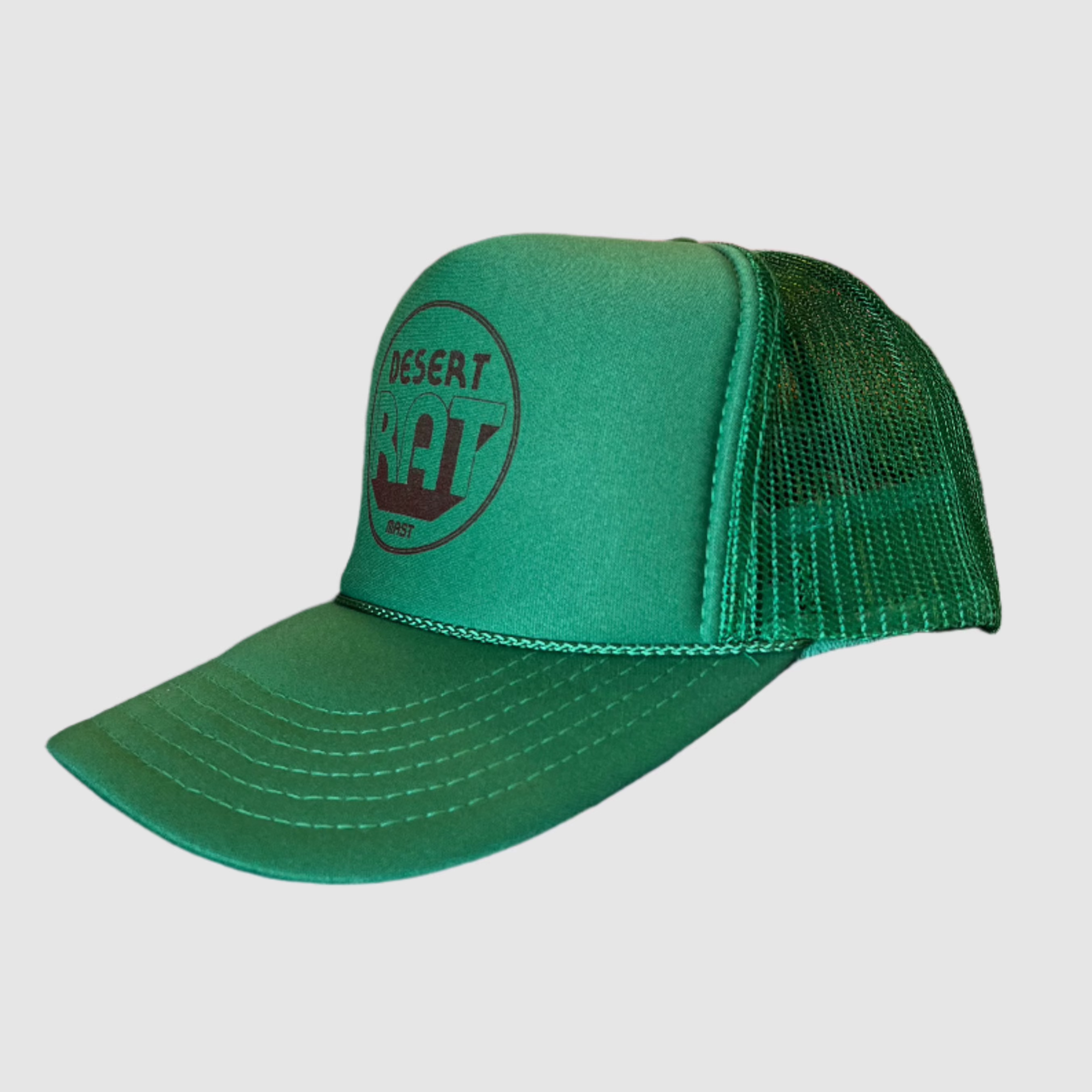 Side view of a classic green truckers cap with polyester foam front and mesh back. "Desert rat" in circular brown print on front of hat with "MAST" printed smaller underneath.