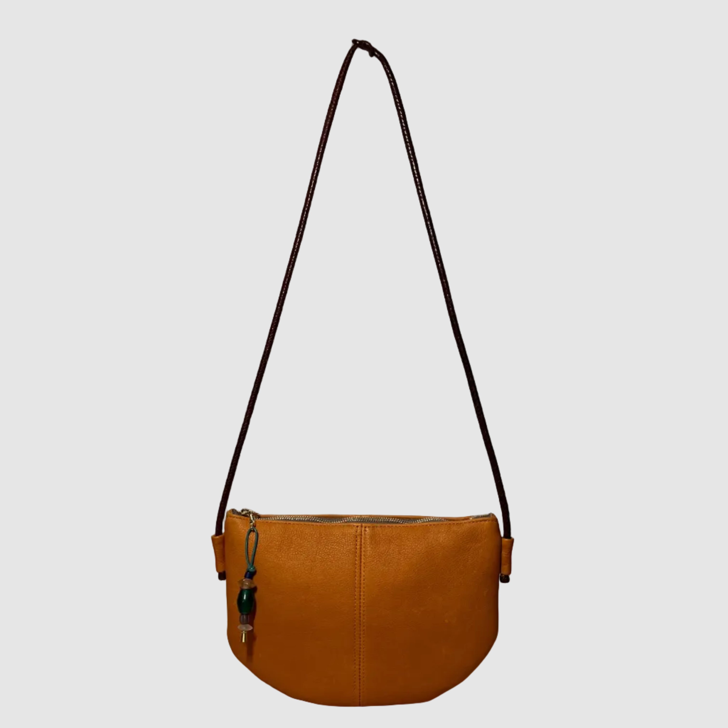 A matte, western, tan leather bag, handmade by Mellow Dawn in Tucson, Arizona. The bag features natural scarring and variation and a dark brown hand woven strap made in Mali. The bag is shown floating on a light grey background.