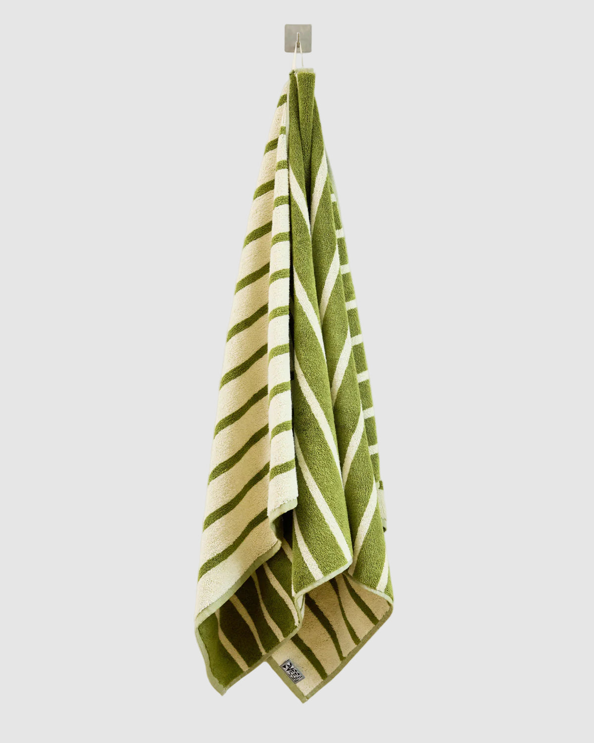 Olive green and beige striped dusen dusen bath towel hanging on a hook on a light grey "wall" background
