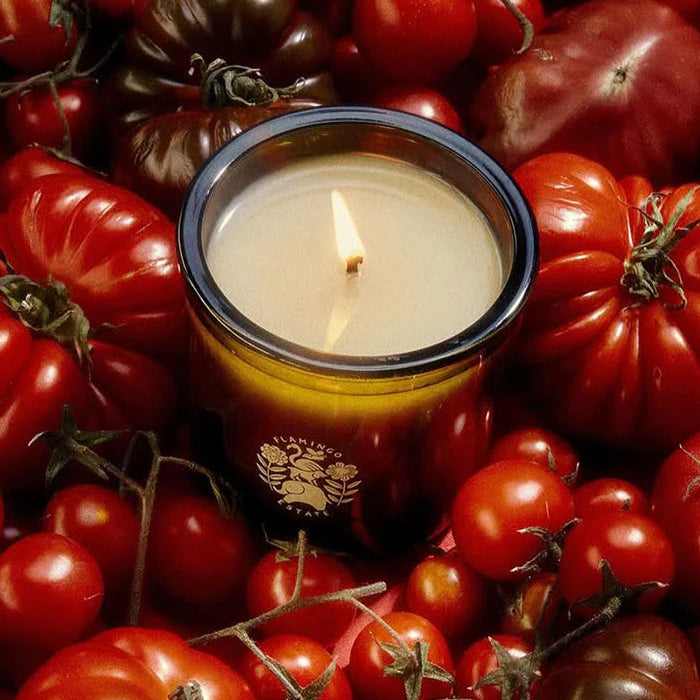 Candle with a logo surrounded by red and brown tomatoes