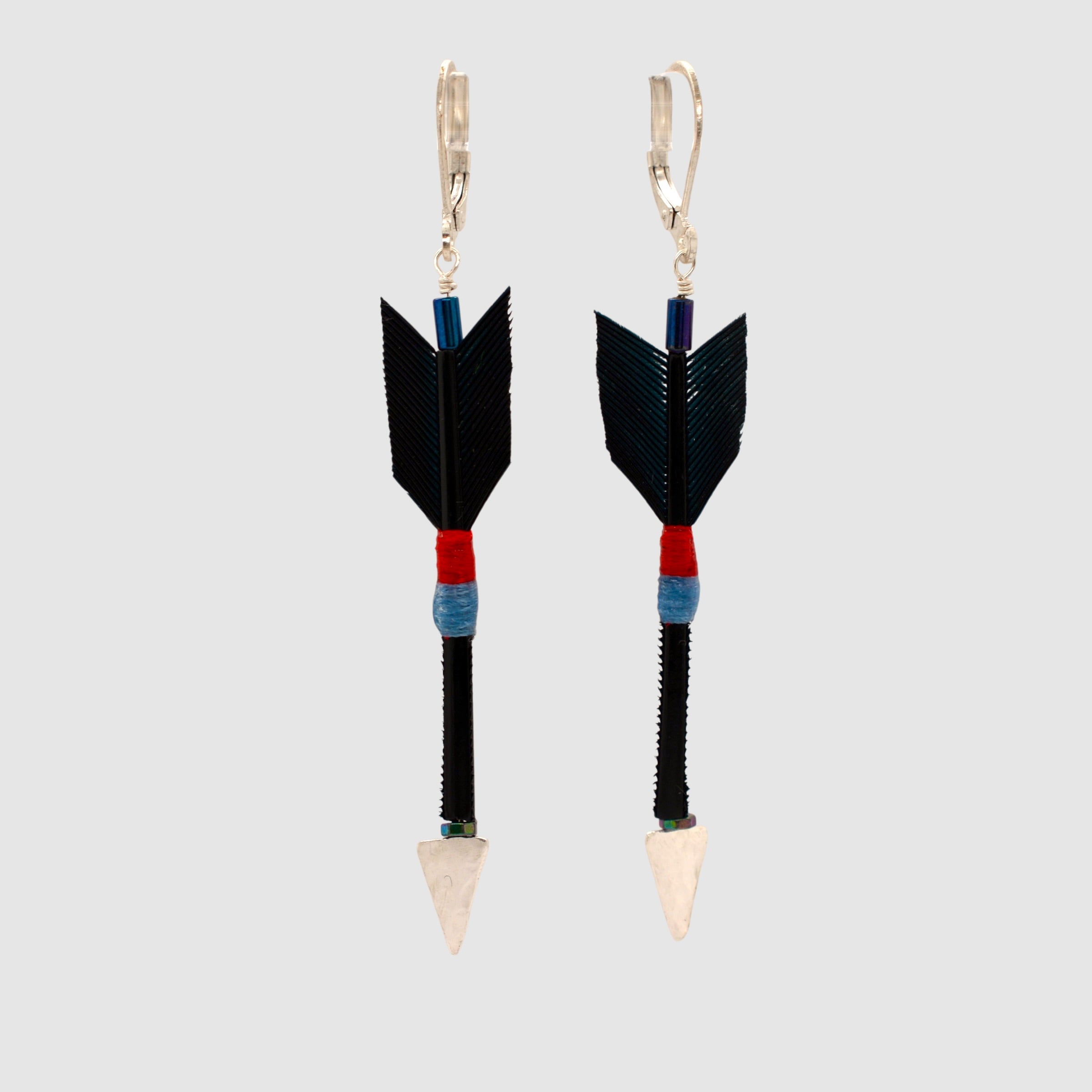 Black feather arrow earrings with sterling silver arrowheads and leverback clasps designed and handmade in Tucson, Arizona by Sofie Albertsen. Displayed on a light grey background.