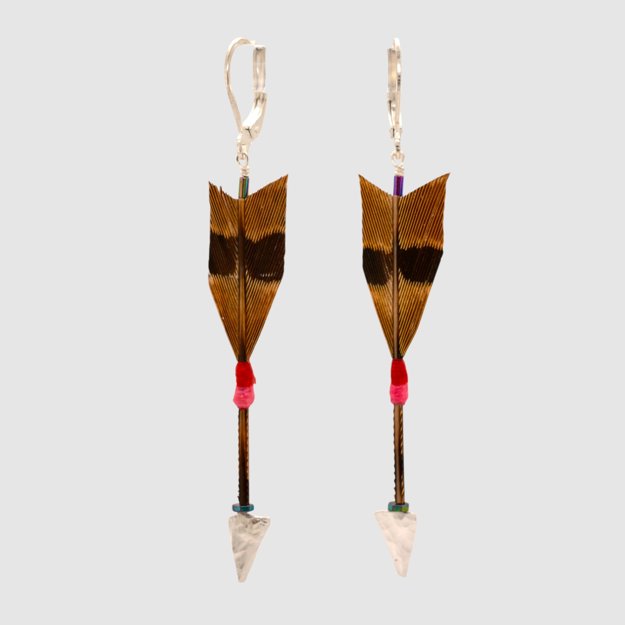 Brown pheasant feather arrow earrings with sterling silver arrowheads and leverback clasps designed and handmade in Tucson, Arizona by Sofie Albertsen. Displayed on a light grey background.