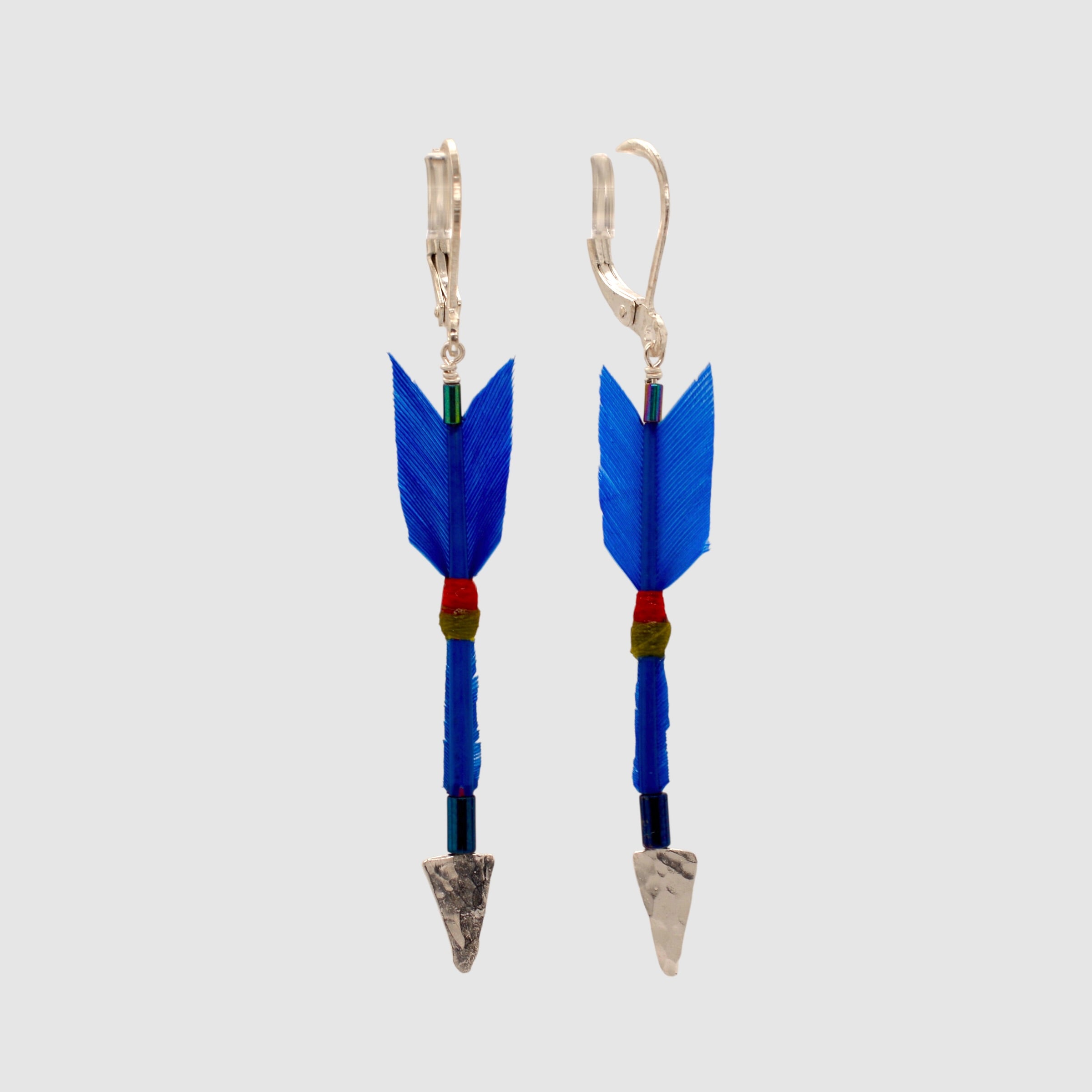 Cobalt blue feather arrow earrings with sterling silver arrowheads and leverback clasps designed and handmade in Tucson, Arizona by Sofie Albertsen. Displayed on a light grey background.