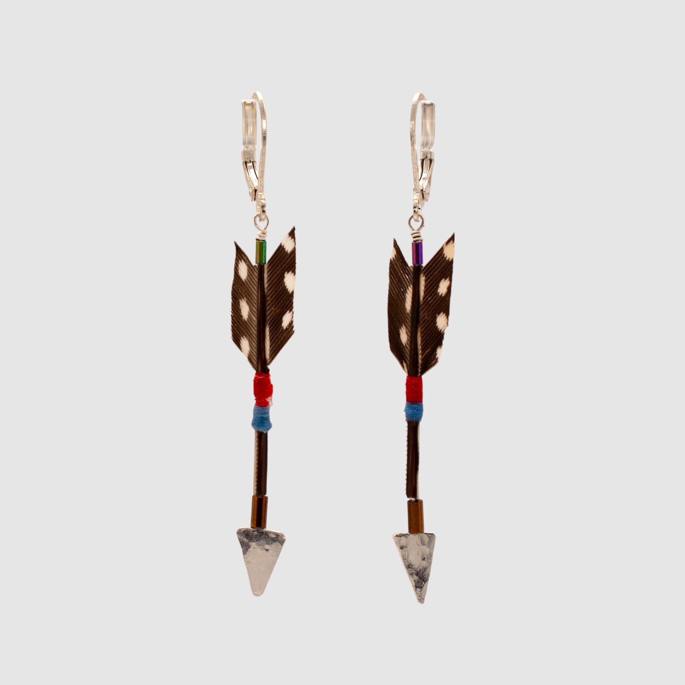 Brown spotted guinea hen feather arrow earrings with sterling silver arrowheads and leverback clasps designed and handmade in Tucson, Arizona by Sofie Albertsen. Displayed on a light grey background.