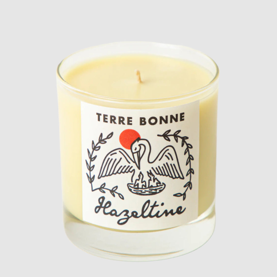 A clear glass candle with a label that has a heron illustration and the text 'TERRE BONNE' and 'hazeltine'.