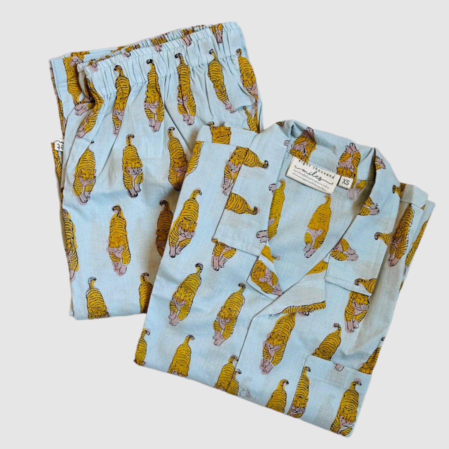 A pair of tiger print pajamas laid out flat, consisting of a button-down top and elastic waist pants with a drawstring.