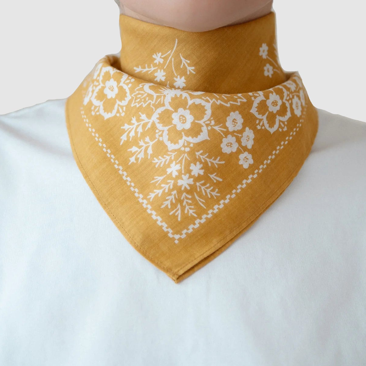 Mustard yellow bandana with white floral embroidery on a white shirt