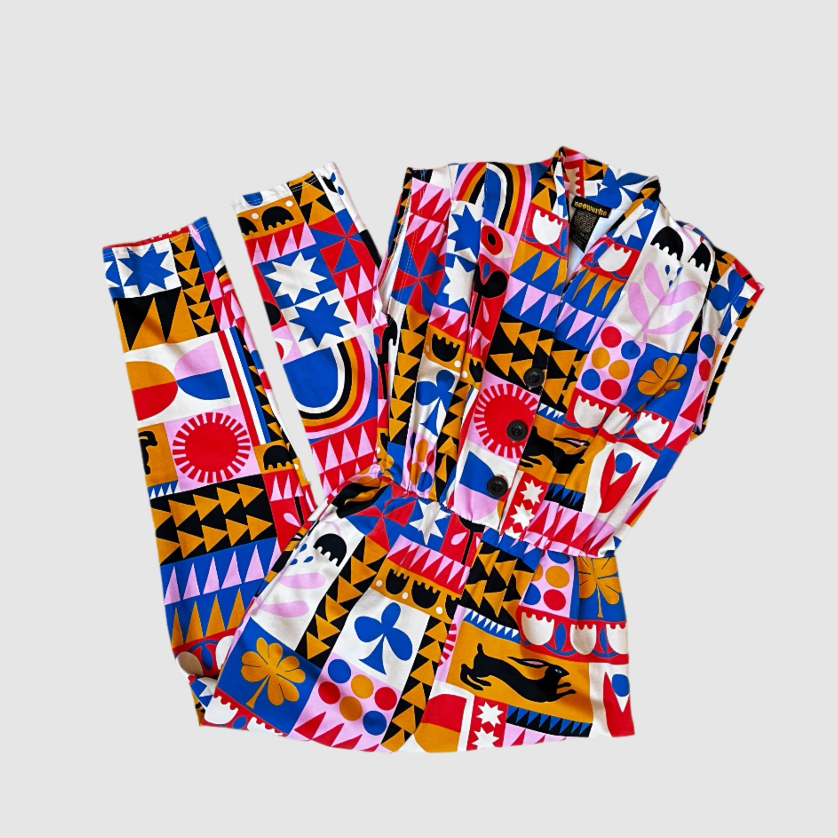 "congdon" style nooworks magic suit folded showing front half and back of legs. Geometric-like pattern of blue, yellow, pink, red, white, and black printed on cotton magic suit. On a light gray background.