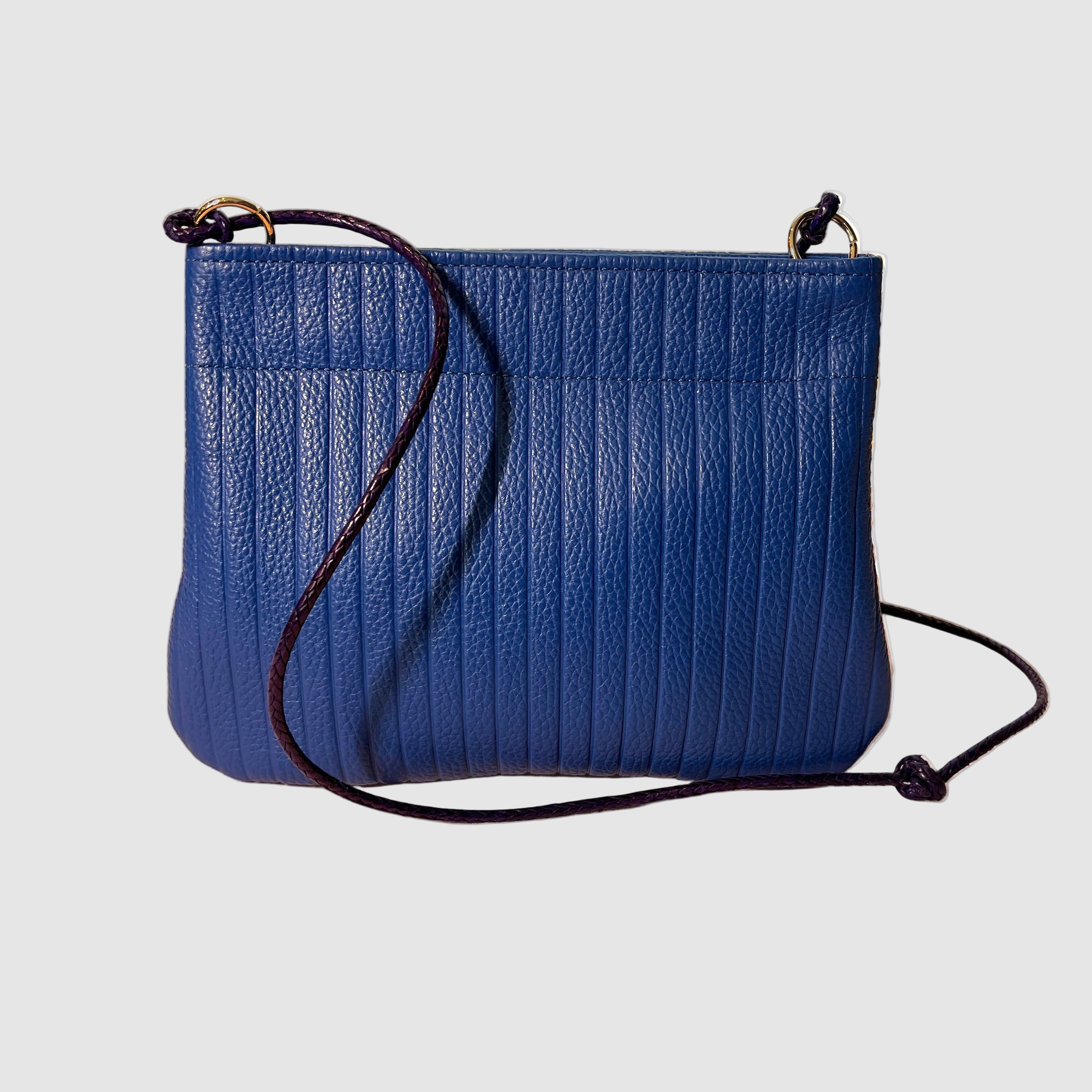 Embossed cobalt blue handmade leather handbag with twisted leather strap on a light grey background. Bag made by Mellow Dawn in Tucson, Arizona.
