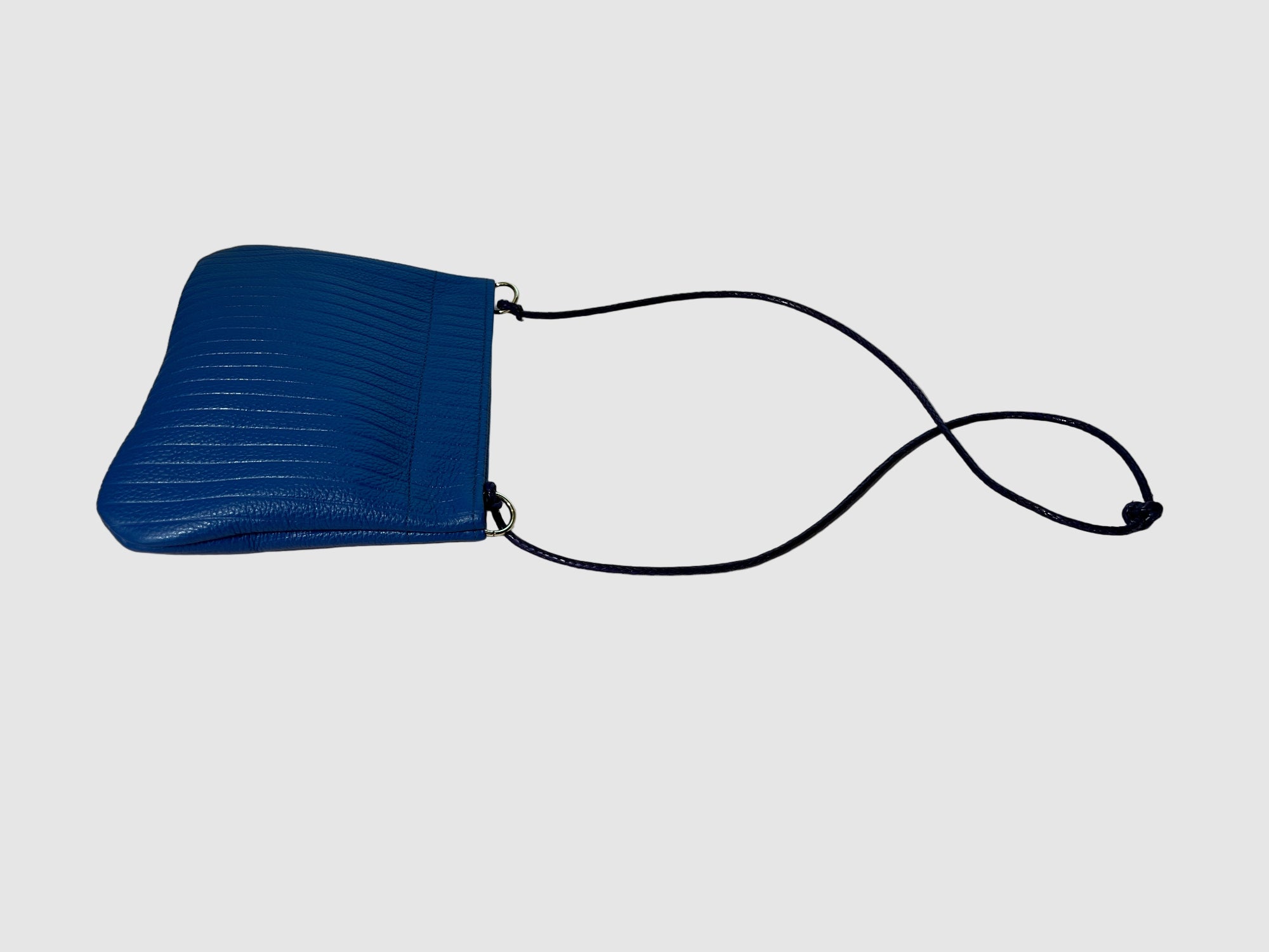 Embossed cobalt blue handmade leather handbag with twisted leather strap on a light grey background. Bag made by Mellow Dawn in Tucson, Arizona.