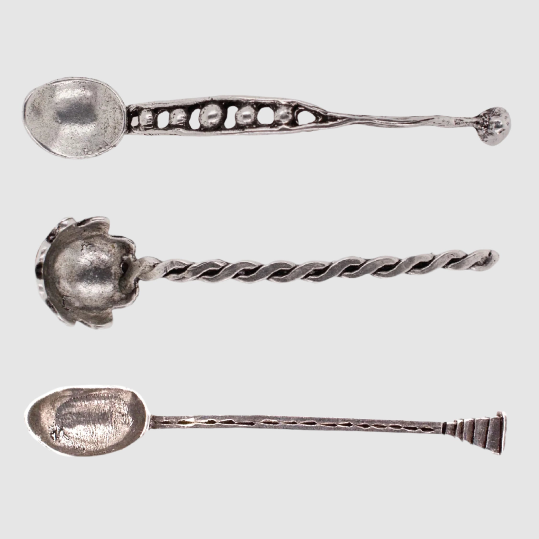 Three silver spoons with decorative handles on a white background