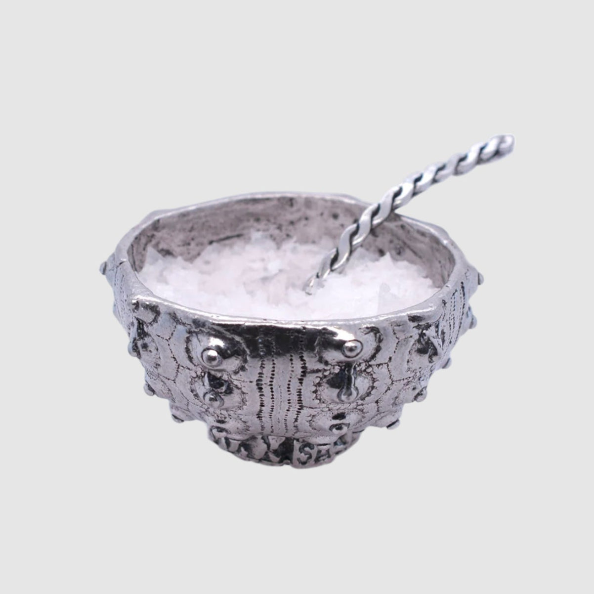 Decorative silver bowl with a spoon on a light gray background