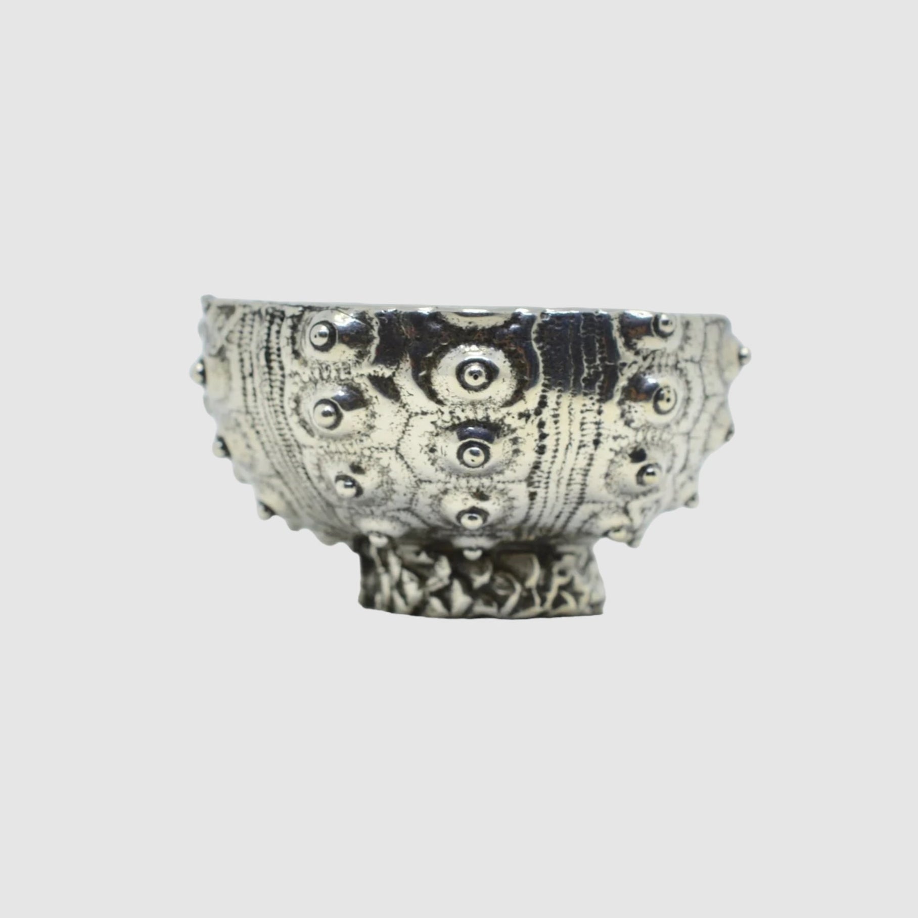 This image features a medium-sized pewter bowl, known as the SEA URCHIN BOWL // SPUTNIK // MEDIUM, crafted by SOFIE ALBERTSEN in Tucson. The bowl stands out with its distinctive sea urchin-inspired patterns etched across its surface, giving it a unique, textured appearance.
