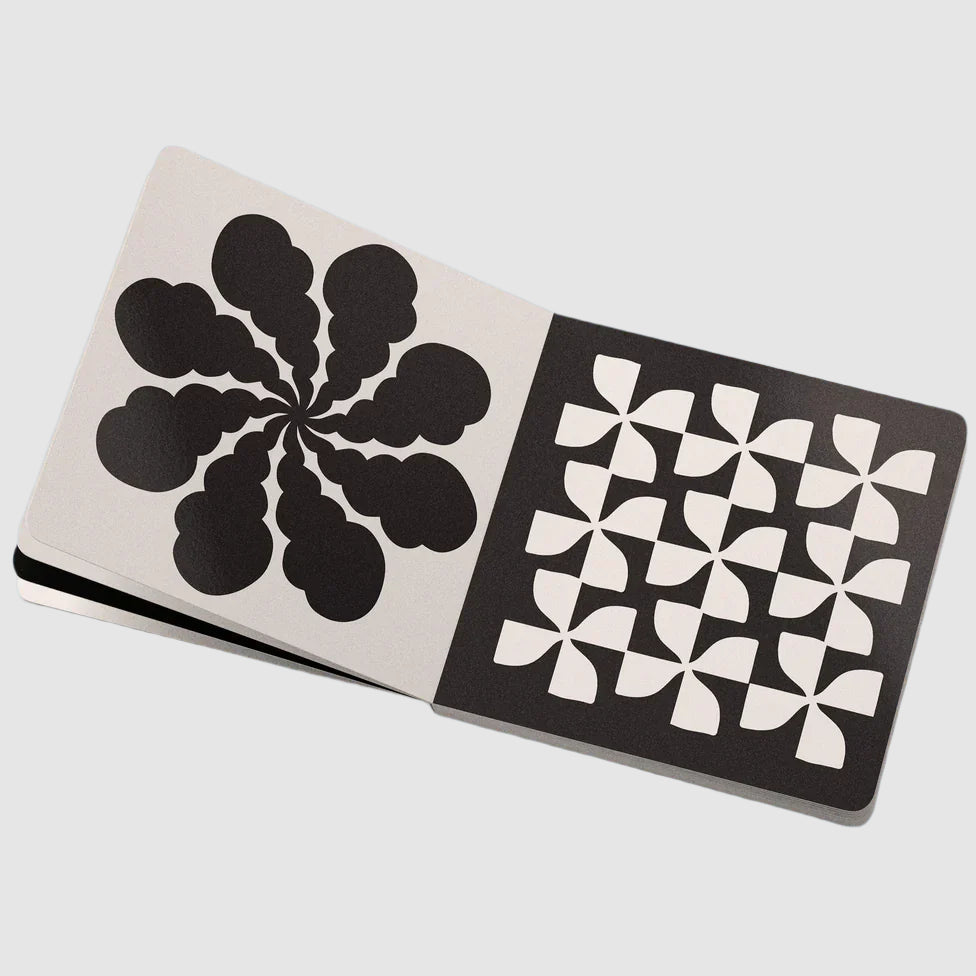 Inside spread of ‘Hi, Baby!’ High Contrast Baby Book by Real Fun, Wow! Left page has a white background with black flower-like symbol centered and large. Right page has black background and a flower-like pattern of 6 centered and large.