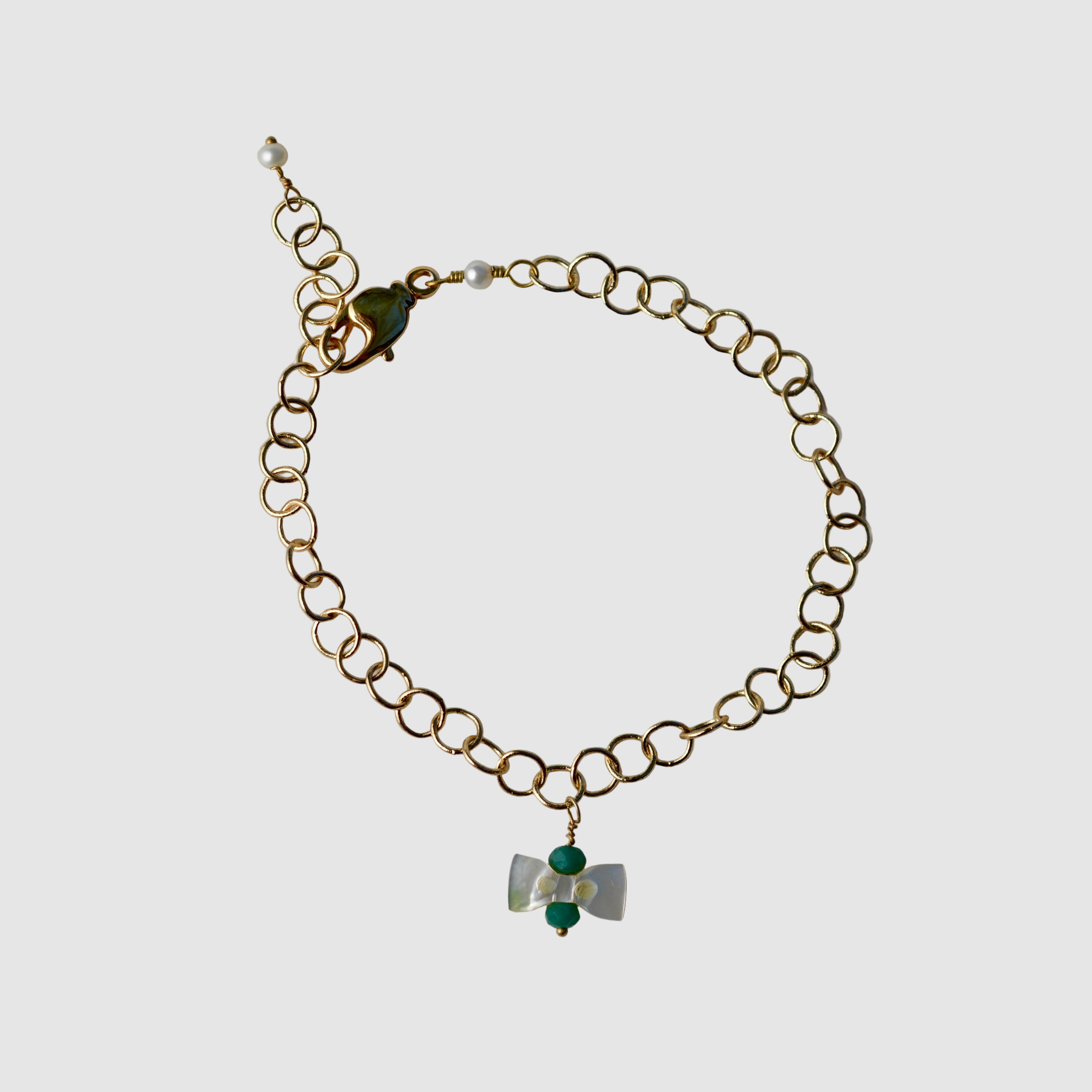Gold chain bracelet with a bow pendant on a light gray background