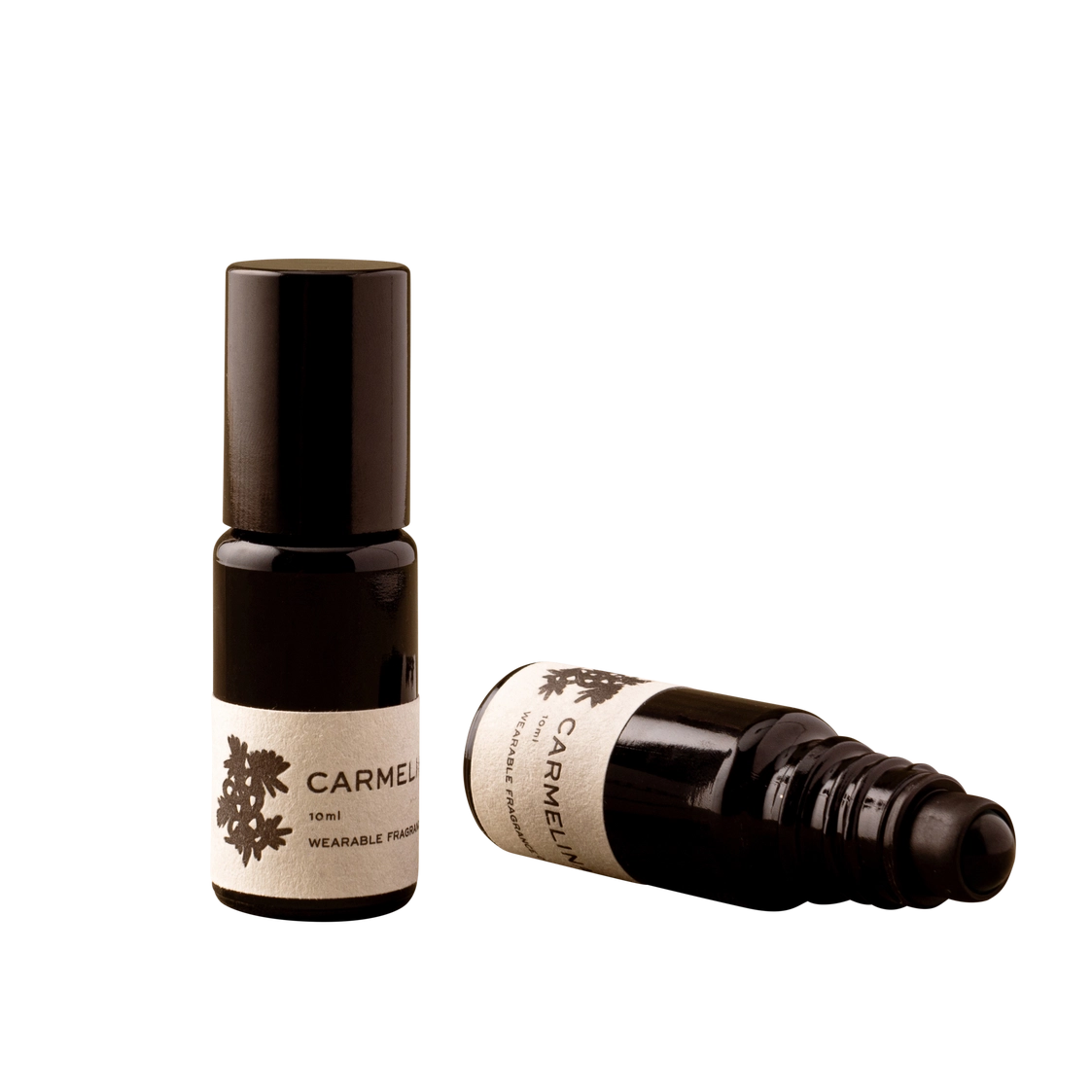Two small dark glass roll-on bottles with cream labels reading CARMEN, one standing upright and one lying on its side, on a plain white background.