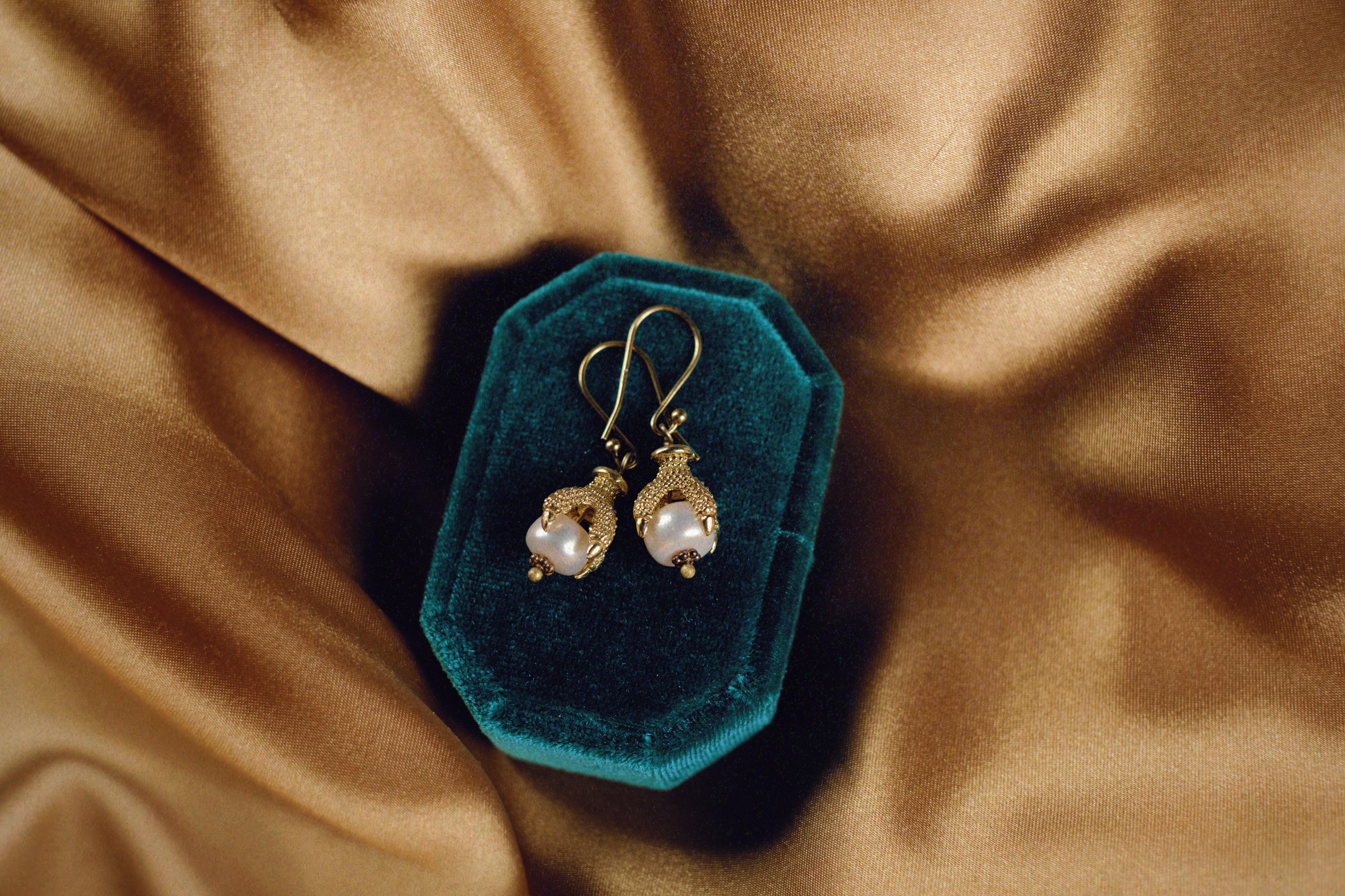 white pearl being clutched in the talons of a gold bird claw. Handmade drop earrings by Tasha Bundy in Tucson, Arizona.