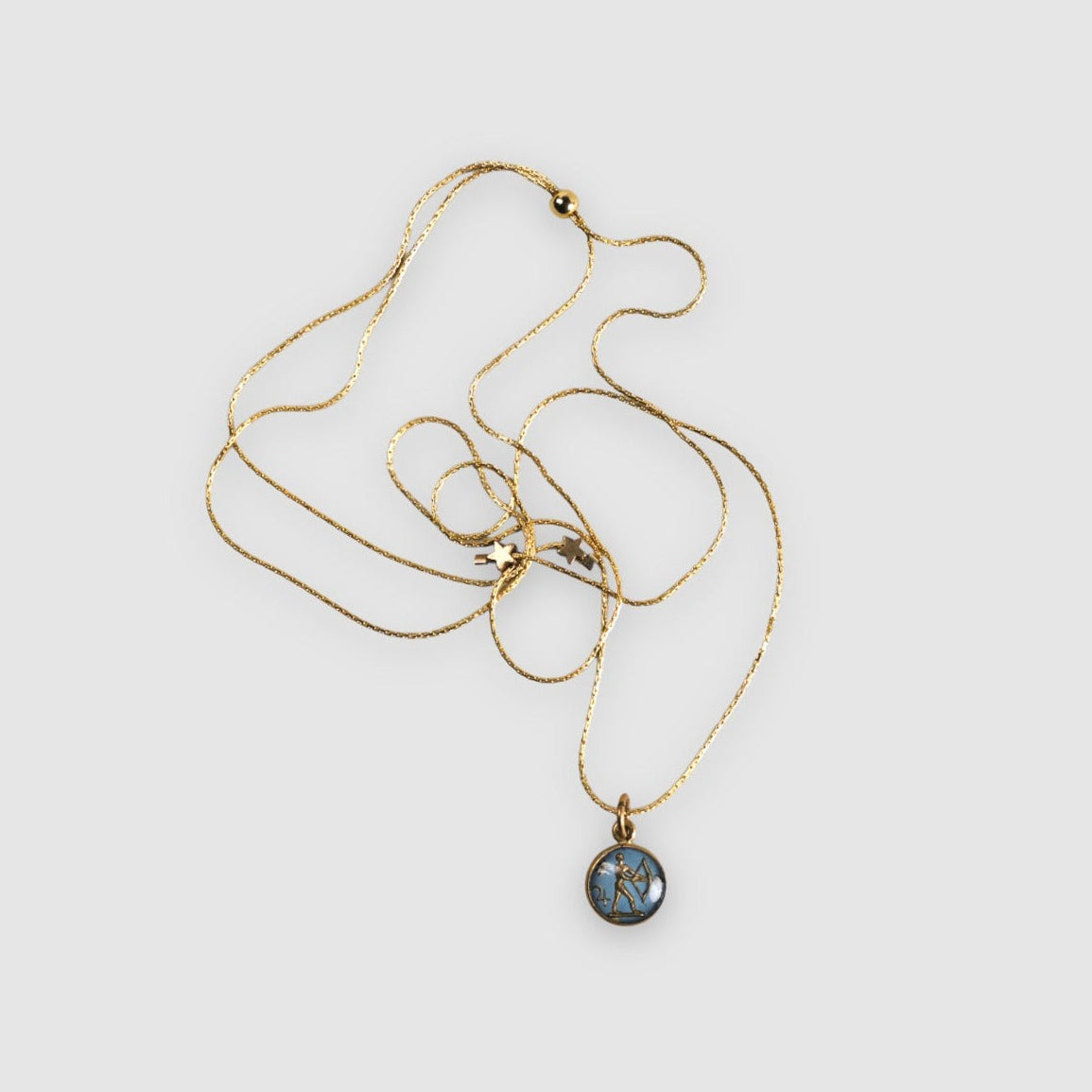 A gold-filled chain necklace with an adjustable clutch closure, featuring a vintage 1950's German Sagittarius Intaglio pendant and tiny brass star accent beads.